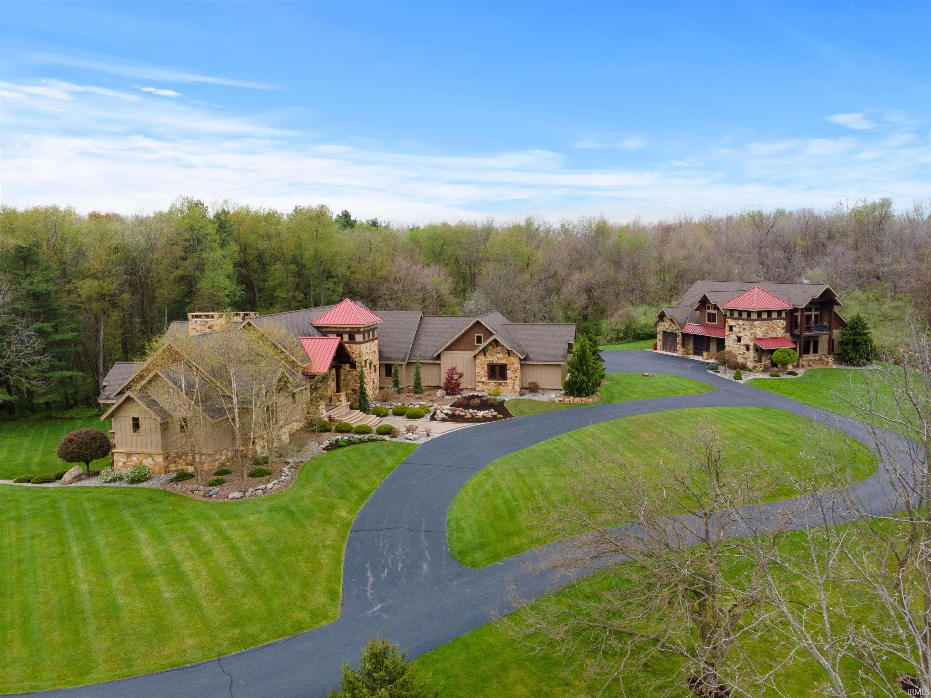 Live your best life in this private, one-of-a-kind country oasis w/12,000+ sq./ft. (2010) custom home and 3,000+ sq/foot Barn-dominium on 59+ partially wooded acres w/1/4-mile paved driveway and 1.3-acre stocked pond. Masterfully designed and crafted, the properties feature natural stone, Indiana-sourced wood for beams, stunning hardwoods, wood ceilings, slate tile, sweeping views, luxury finishes at every turn, pro landscape/hardscape (irrigated w/LED lighting), and state-of-the-art technology. The main home features open concept living w/2-story beamed timber-frame ceilings and floor-to-ceiling windows, 2-story stone fireplace + large dining area. The chef's kitchen boasts double granite islands, instant hot water, 6- burner/griddle Wolf cooktop + double Wolf wall ovens, Subzero oversized side-by-side, gracious walk-in pantry, 2 Asko dishwashers, & stunning custom built-ins. French doors lead to the timber-frame screened porch w/slate floors, 2-story stone fireplace, built-in stone grill, stunning views. The primary en-suite boasts a private balcony, oversized walk-in stone shower + copper accents, double vanity w/granite/stone, enormous walk-in closets & is cleverly connected to laundry room & mud-rooms. Off the foyer, a stone accented hallway leads to BRs 2 & 3, both large w/ stone/tile ensuites, walk-in closets and 12' ceilings, and the library (4th BR) w/private balcony, en-suite, and fabulous built-in shelves + desk. Don’t miss the 2nd story loft overlooking foyer and great rooms (more views!) w/ game/lounge area in the middle and doors on either end to walk-in floored attic (*future bedrooms). The finished walk-out lower level is an entertainers' paradise - 12-ft. ceilings, chef’s kitchen w/granite bar (seating for 6), open to living/game room w/stone fireplace. Sliders lead to fabulous covered outdoor space w/hot tub, 2-way stone fireplace, outdoor TV (*future pool). A large guest suite, tricked-out theatre room, fitness room, safe room (“Fort Knox”), and half bath complete the lower level. The detached Barn-dominium boasts 4 extra-long tandem bays (8+ car temperature-controlled), dog run, heated workshop (built-ins + epoxy floor), half bath, laundry room & mud room on the main level. Upstairs, 1700+ sq. ft., 2 BR/1 BA (dual shower + double vanity), luxury living area (slate, hardwoods, stone, granite) w/open concept, stone fireplace, and vaulted wood ceiling w/reclaimed wood beams. Security tied to main house + wired for sound.