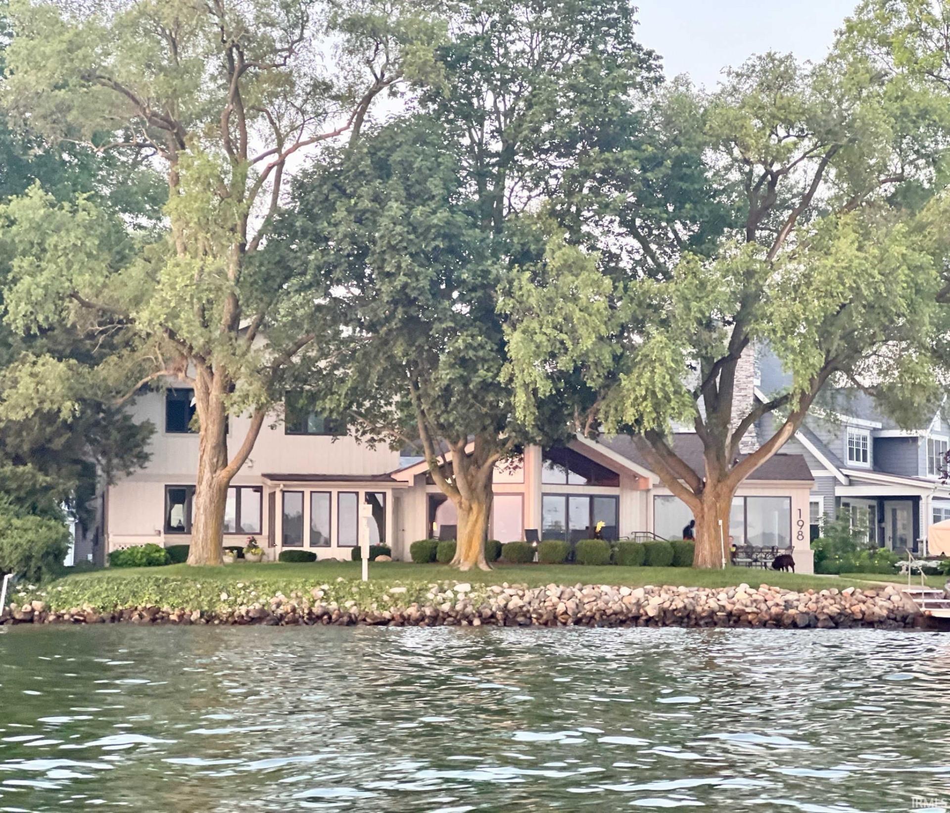 Welcome to a charming home located on Lake Wawasee, a 3,064 acre ski lake. This home features updated bathrooms and in 2023, new windows, flooring and paint. This home boasts a timeless design that exudes warmth and character. With 139 feet of lake frontage on a slight peninsula, this allows for a 270 degree view of the water. It is southwest facing and provides cool breezes and  sunsets, as well as unique privacy from neighbors.    The interior of the home is thoughtfully designed with a seamless flow between the living spaces. The main level features two living spaces, cozy dining area, well-appointed kitchen with modern appliances and primary suite.  Enjoy your favorite beverage in the all seasons room.  Upstairs, you will find 4 bedrooms, each offering ample light and closet space.  Two full bathrooms and a large storage room complete this area. This property includes a modern boathouse built on 20 feet of channel frontage behind the home. The lower level has two boat wells, and provides storage for water toys. The upstairs has a small living room, two bunk rooms and a full bath. This space can easily accommodate an additional 10 guests.    Outside, the property is surrounded by lush landscaping and mature trees, creating a serene oasis. The patio has been designed to take advantage of the view which could be argued as one of the best on Lake Wawasee.  If you know much about Wawasee, this is truly one of a kind.   Don't miss the opportunity to make this lovely property your new lake place for years to come!