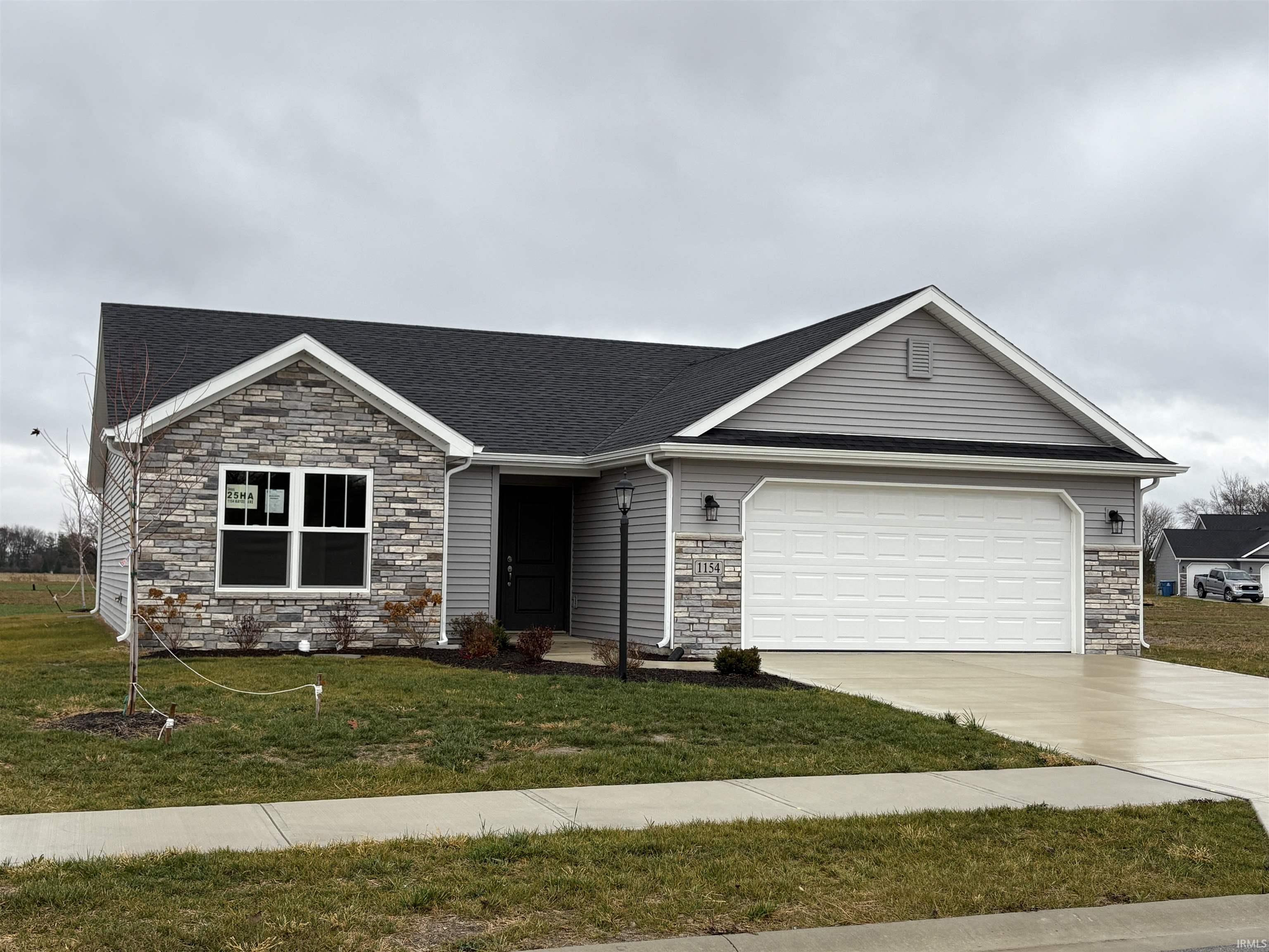 Ranch-style house featuring stone siding, concrete driveway, and a front lawn