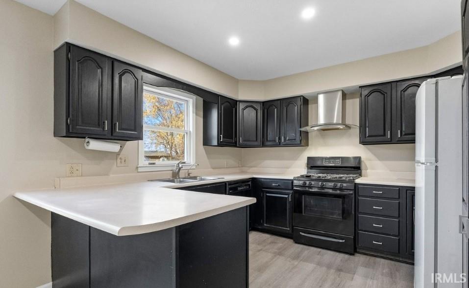 Kitchen featuring dark cabinets, gas stove, light countertops, wall chimney exhaust hood, and a peninsula