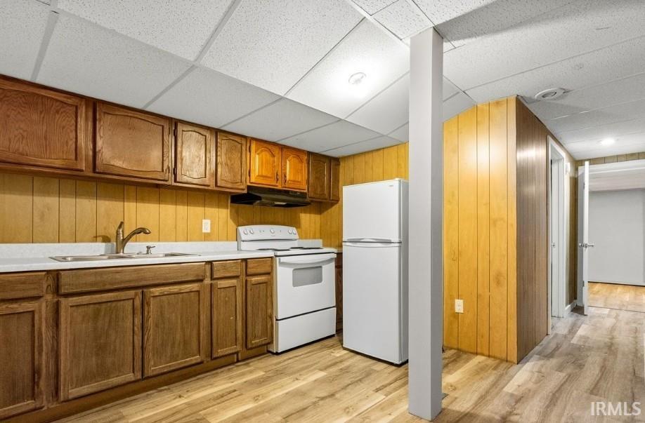 Kitchen with brown cabinets, wood walls, white appliances, a drop ceiling, and light countertops