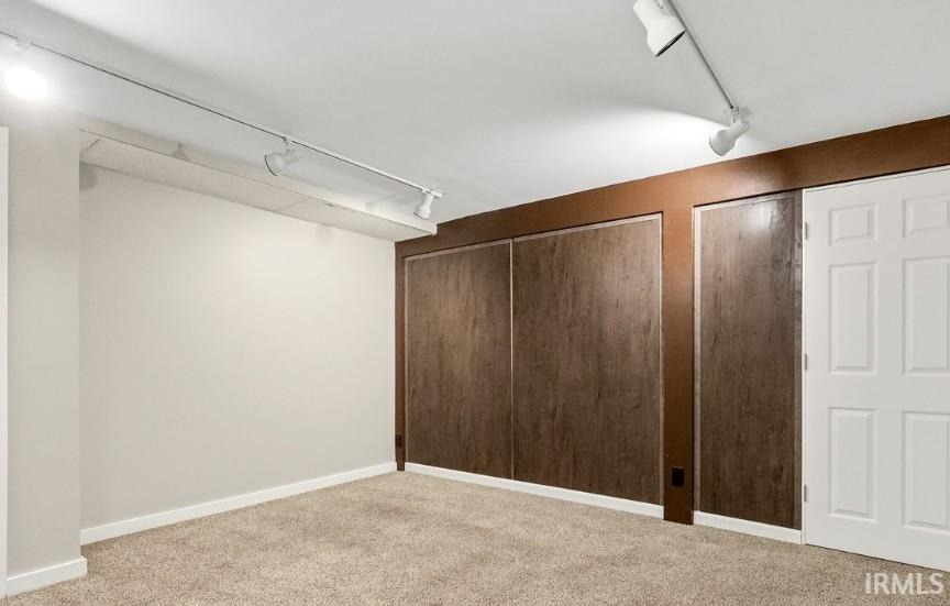 Unfurnished bedroom with rail lighting, light carpet, and multiple closets