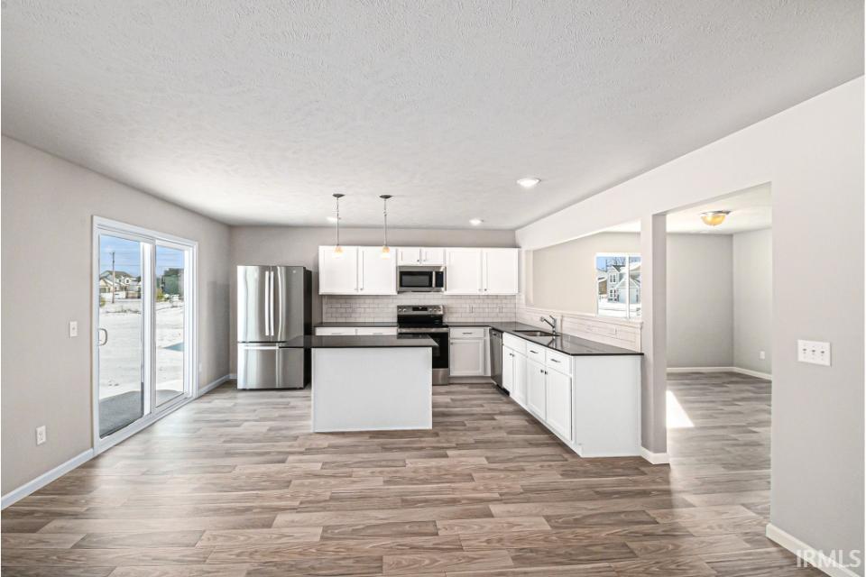 The kitchen includes a center island for additional storage and prep space.  The extended edge can fit barstools and there is pendant lighting above. Quartz counters are accented by subway tile backsplash and select stainless steel appliances are included