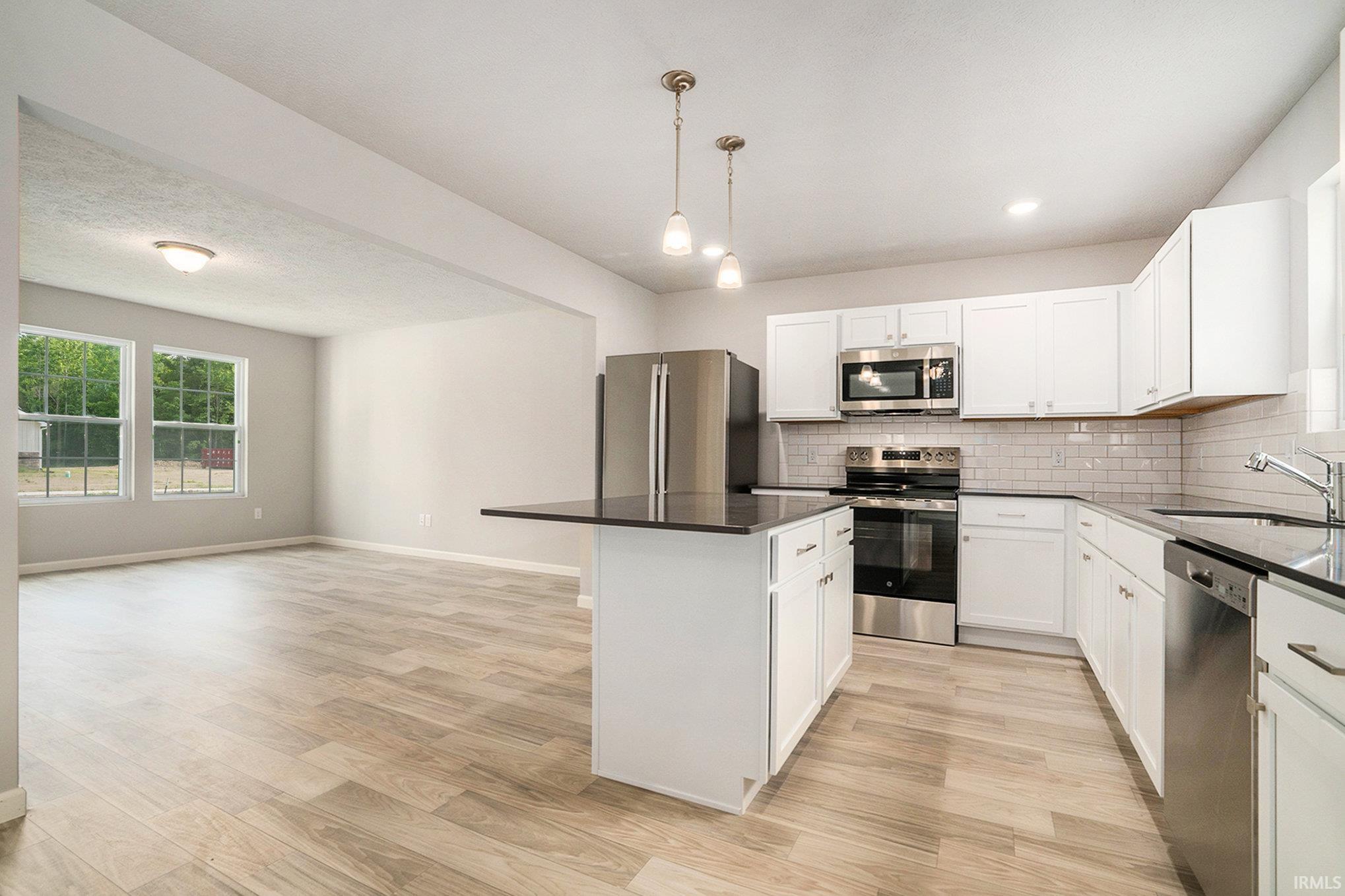 The kitchen includes a center island with extended seating and pendant lighting above.  Quartz counters are accented by subway tile backsplash. Stainless steel appliance package included.
