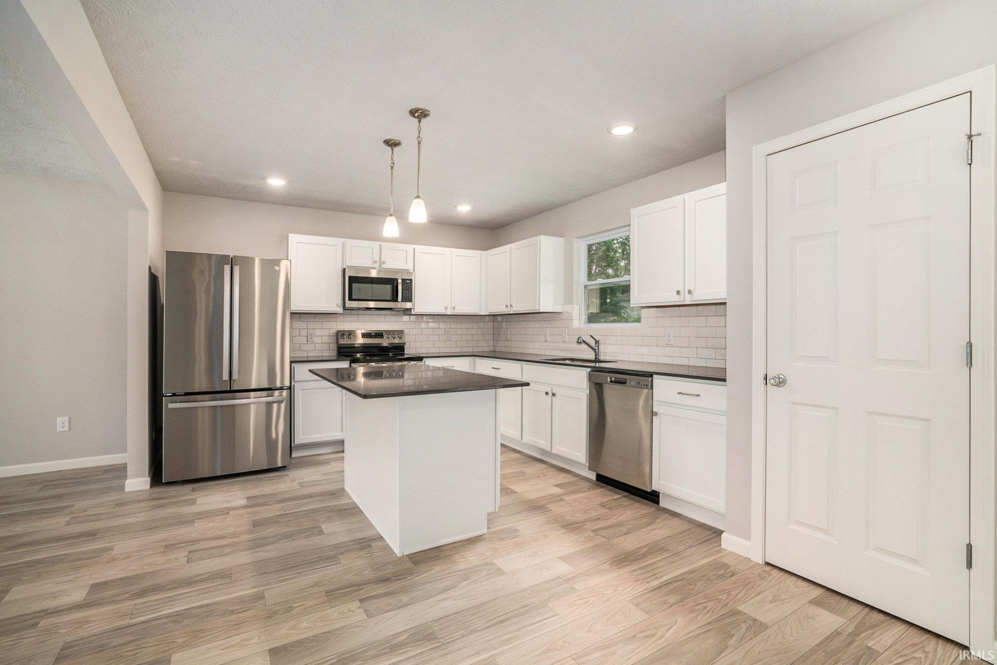 The kitchen includes a center island with extended seating and pendant lighting above.  Quartz counters are accented by subway tile backsplash. Stainless steel appliance package included.