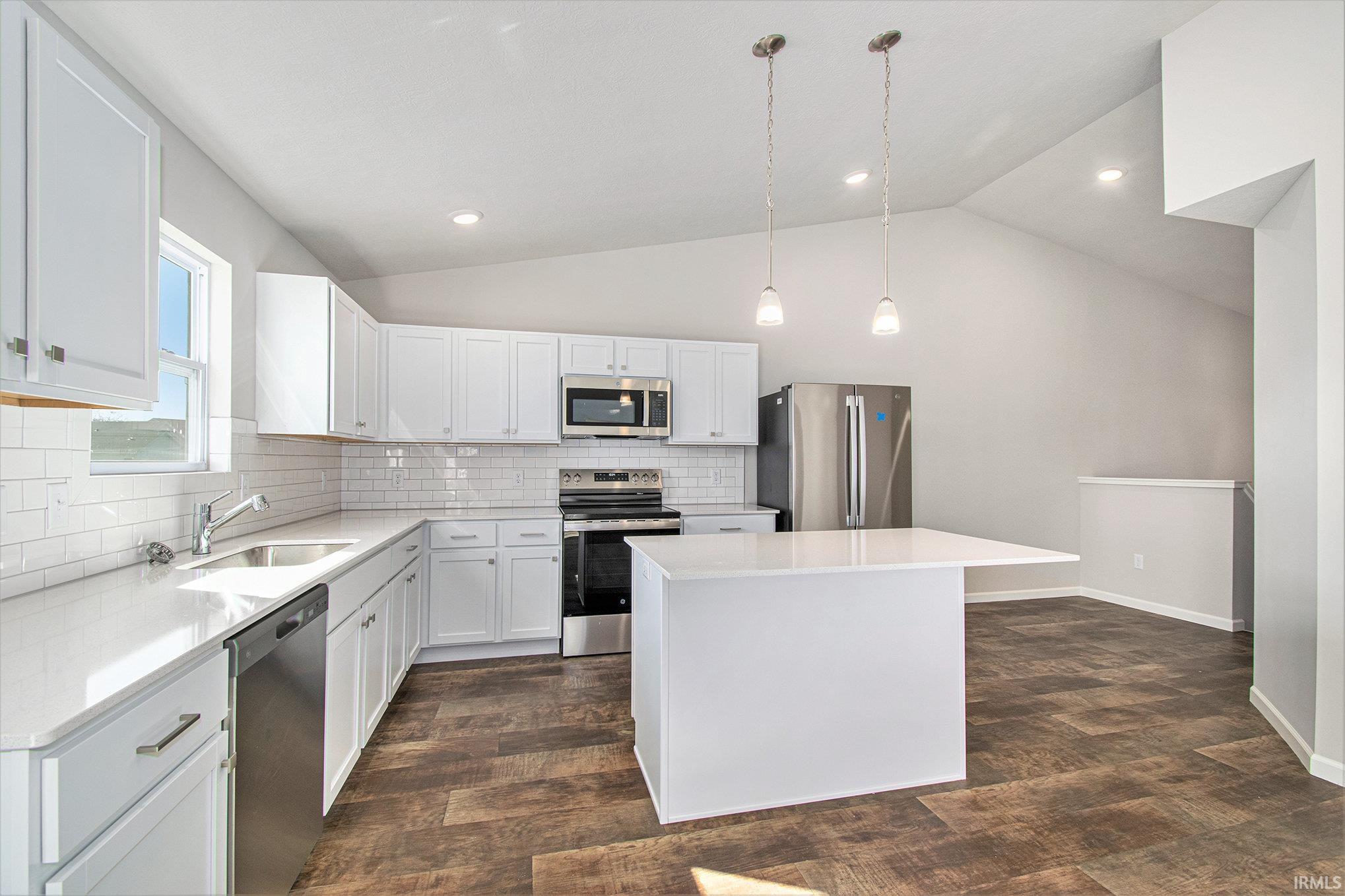 The kitchen features quartz counters with subway tile backsplash, a large center island for additional prep space and storage, accented with pendant lighting above and stainless-steel appliances.