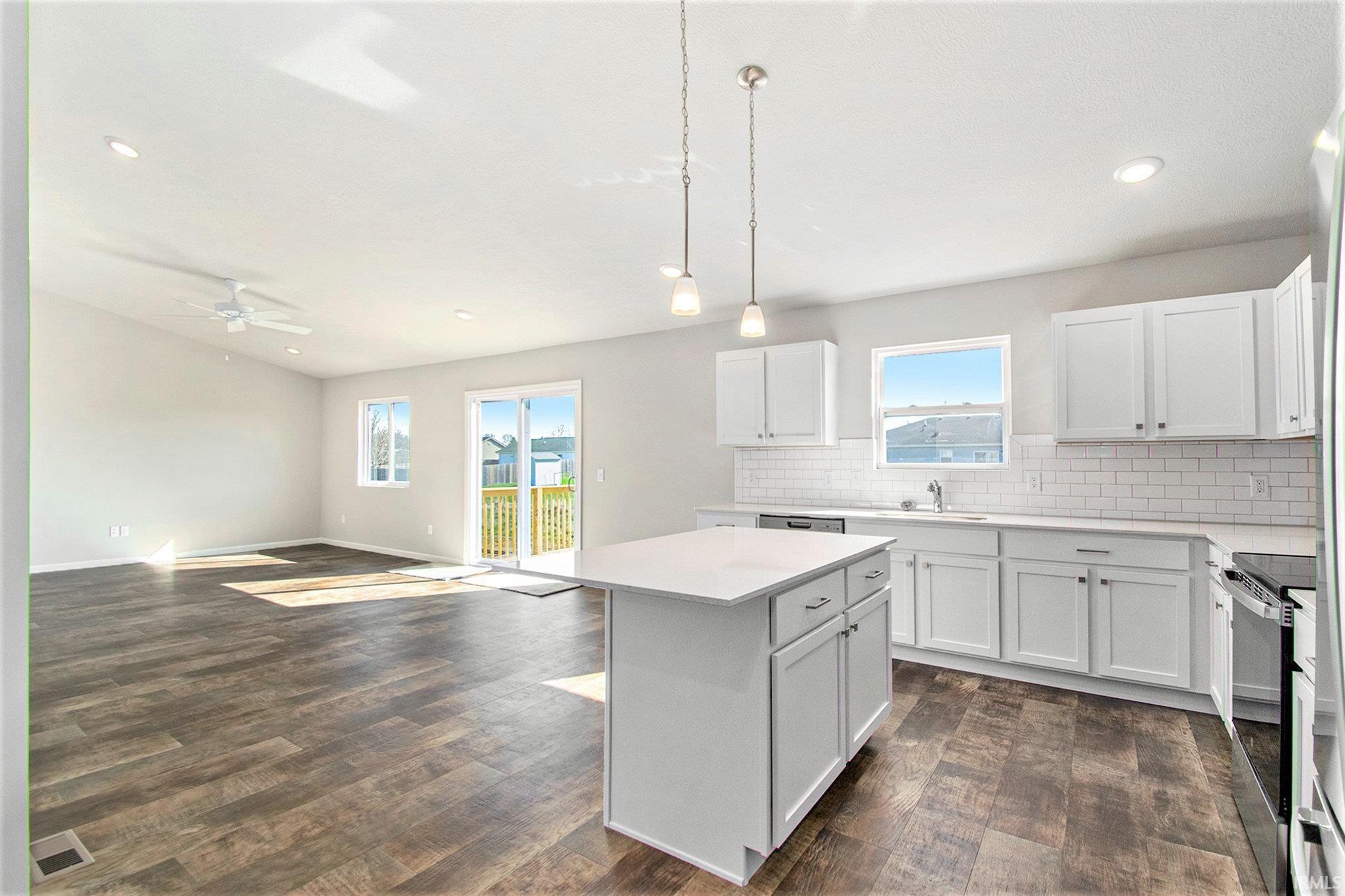 The kitchen features quartz counters with subway tile backsplash, a large center island for additional prep space and storage, accented with pendant lighting above and stainless-steel appliances.