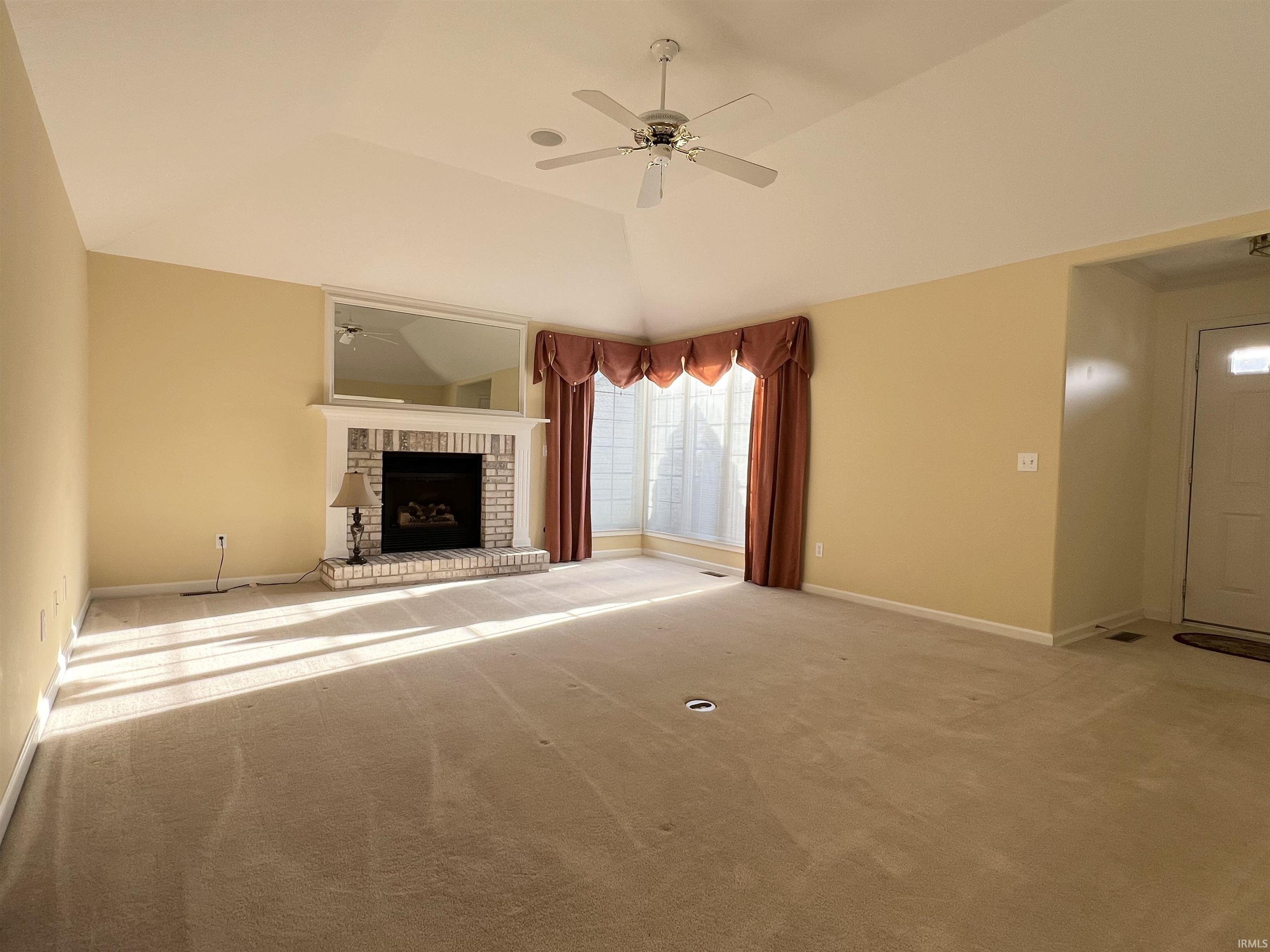 Unfurnished living room featuring a brick fireplace, light carpet, a ceiling fan, and vaulted ceiling