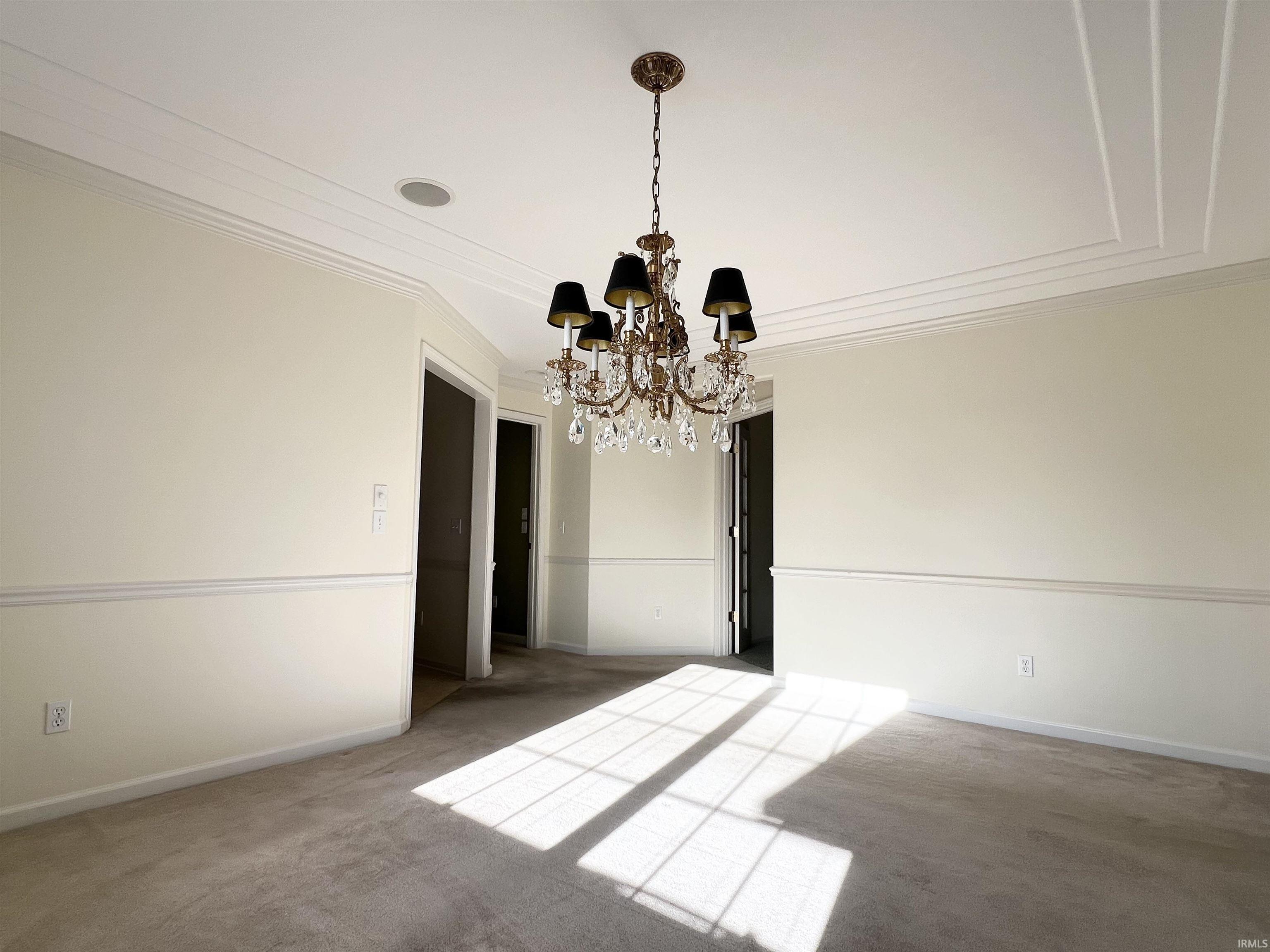 Empty room with a chandelier, crown molding, and carpet flooring