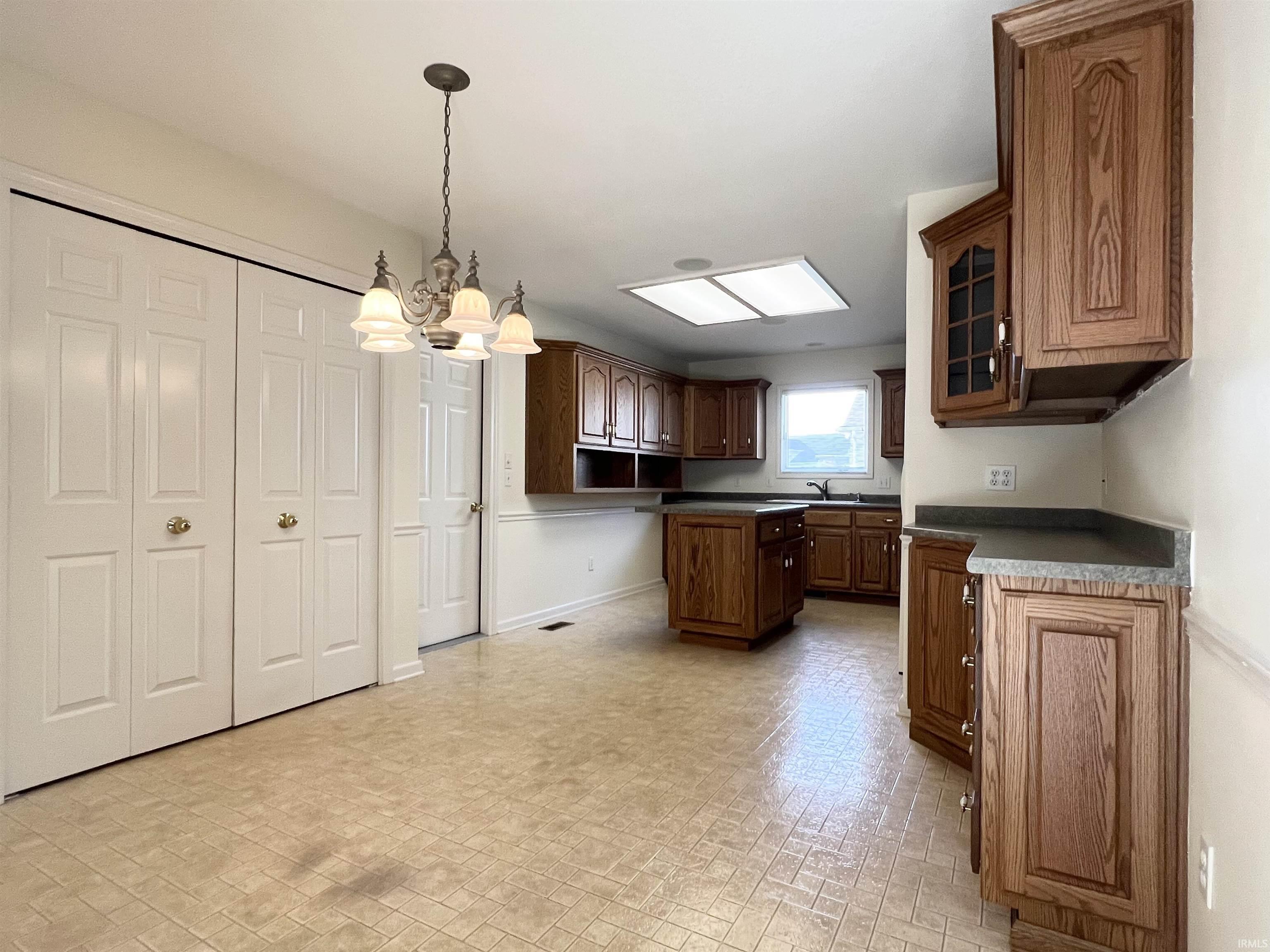Kitchen with brick patterned floors, hanging light fixtures, glass insert cabinets, a chandelier, and dark countertops