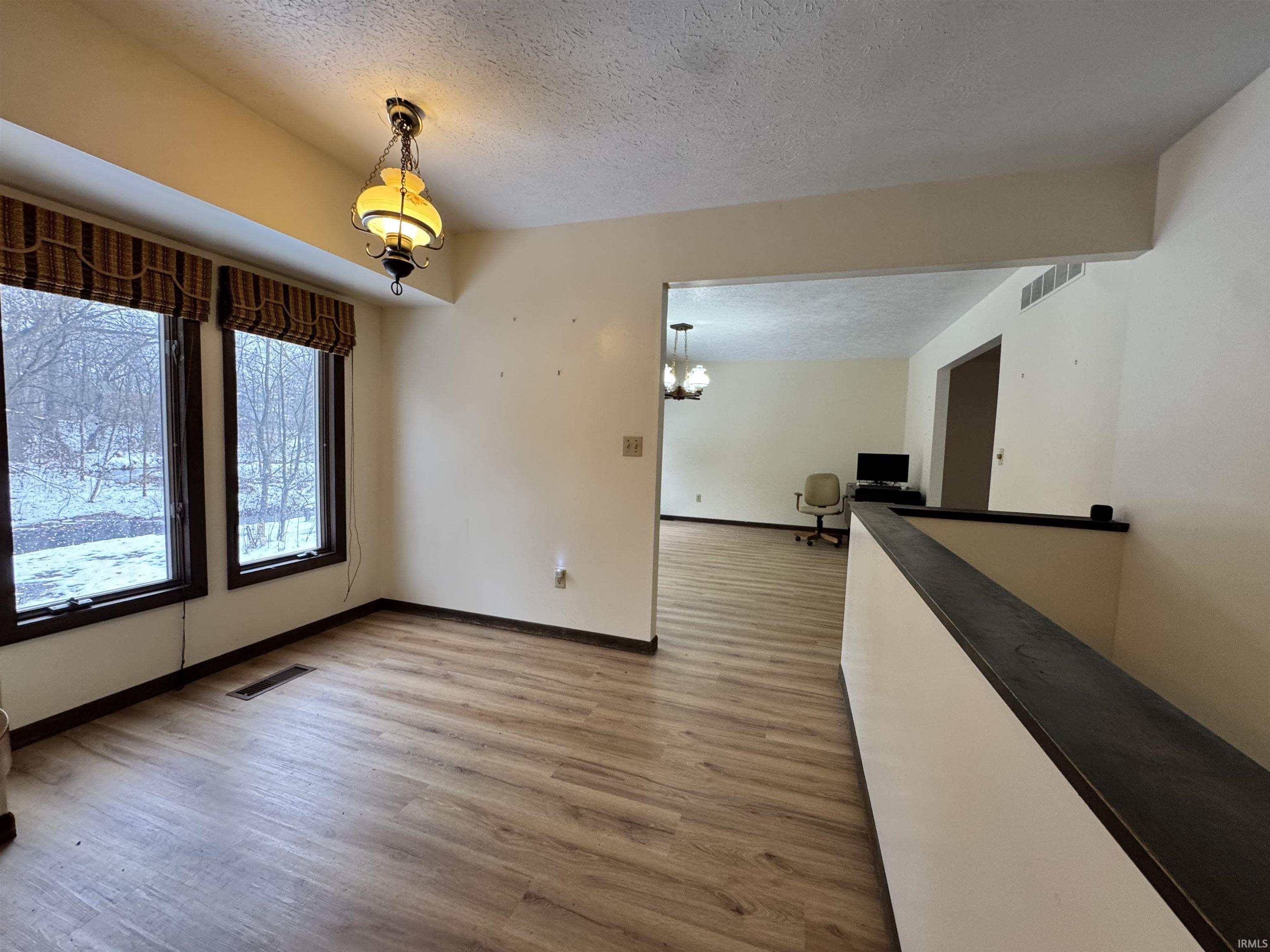 Empty room featuring a textured ceiling, light wood-style floors, and a chandelier