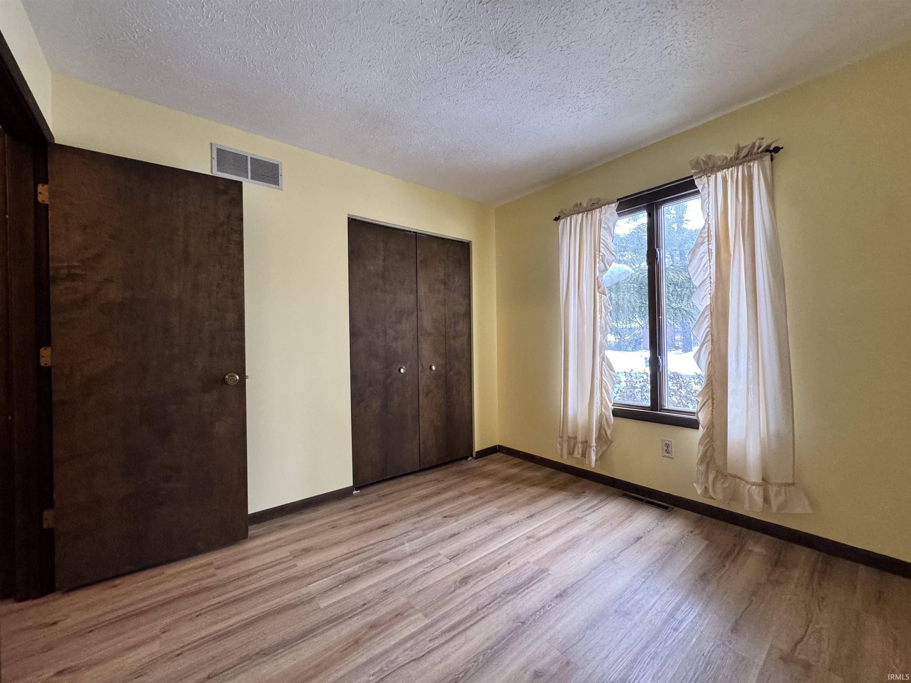 Unfurnished bedroom featuring a textured ceiling, light wood finished floors, and two closets