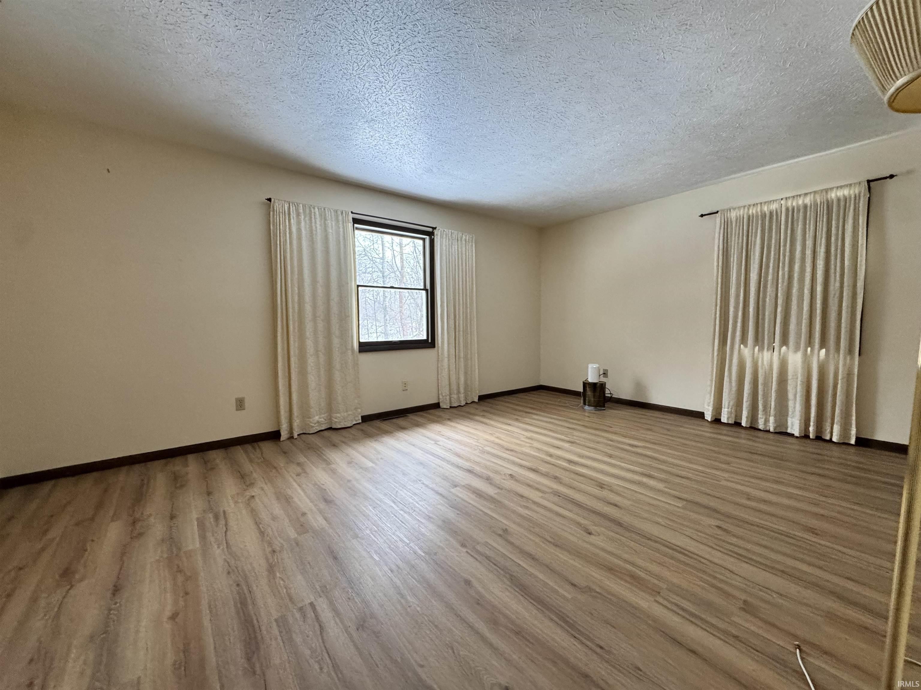 Empty room featuring light wood-type flooring and a textured ceiling