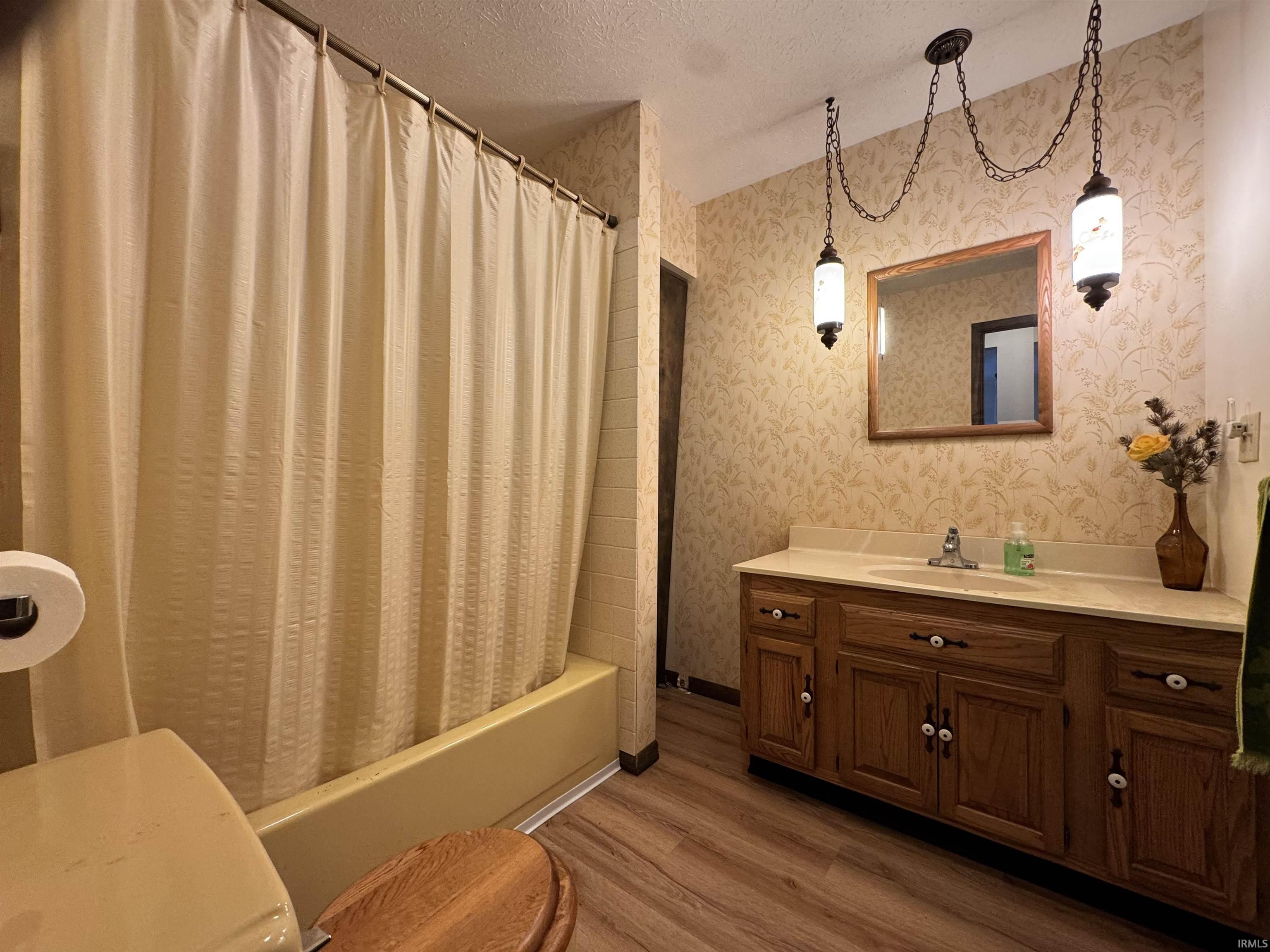 Full bath with a textured ceiling, vanity, shower / tub combo, wallpapered walls, and wood finished floors