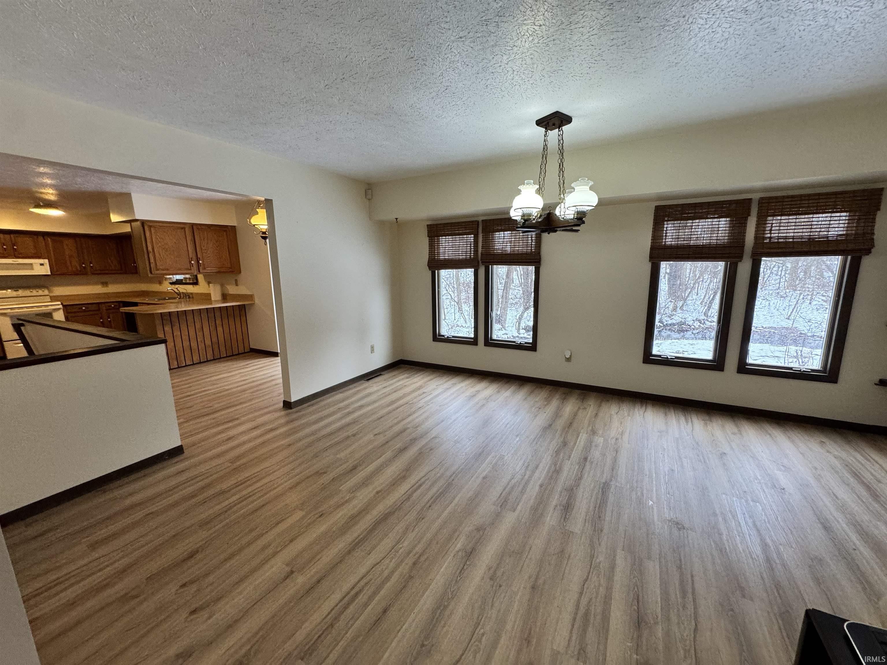 Unfurnished living room featuring a textured ceiling, a chandelier, and light wood-style flooring