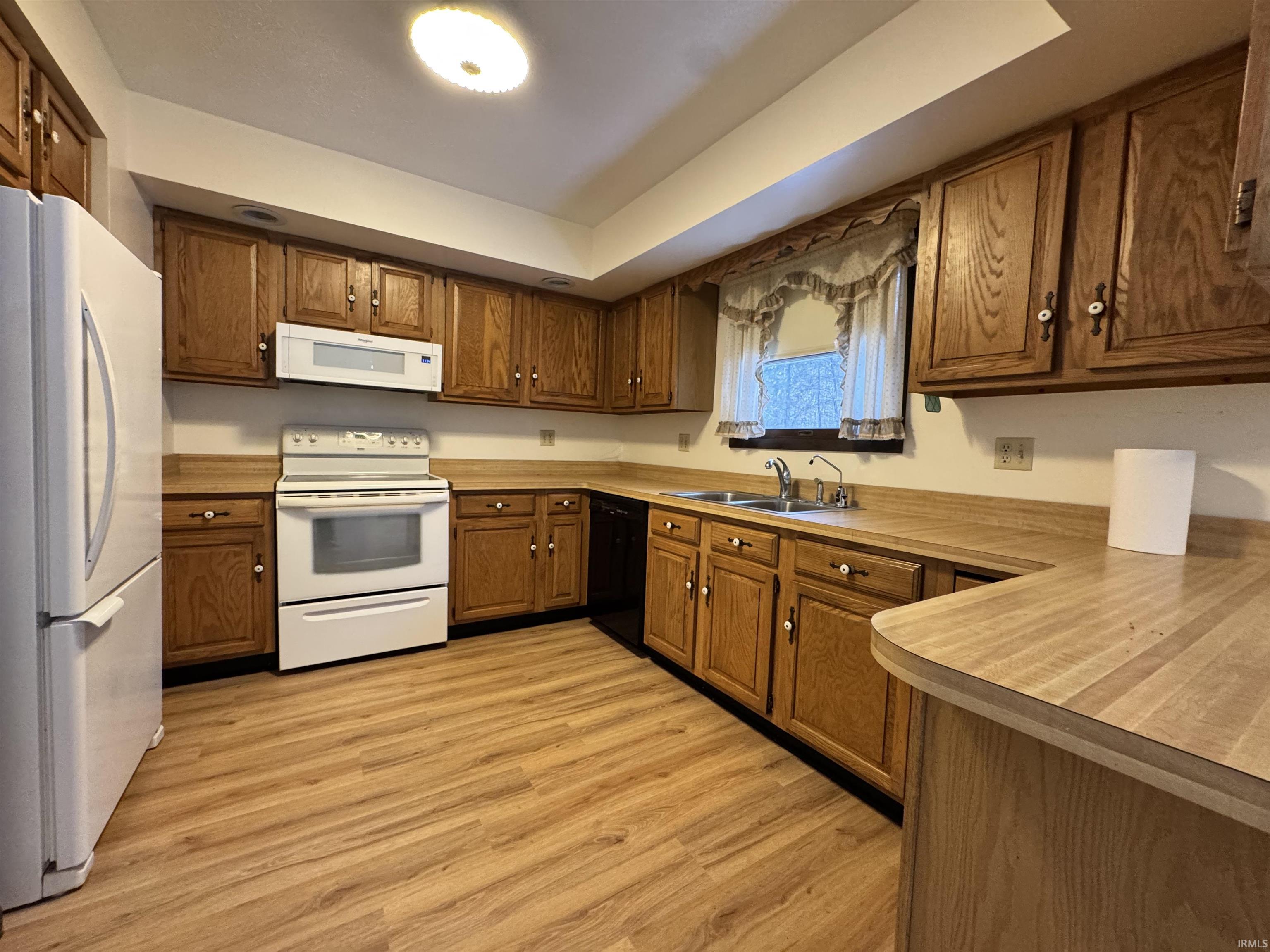 Kitchen with white appliances, light wood-style flooring, light countertops, brown cabinetry, and a tray ceiling