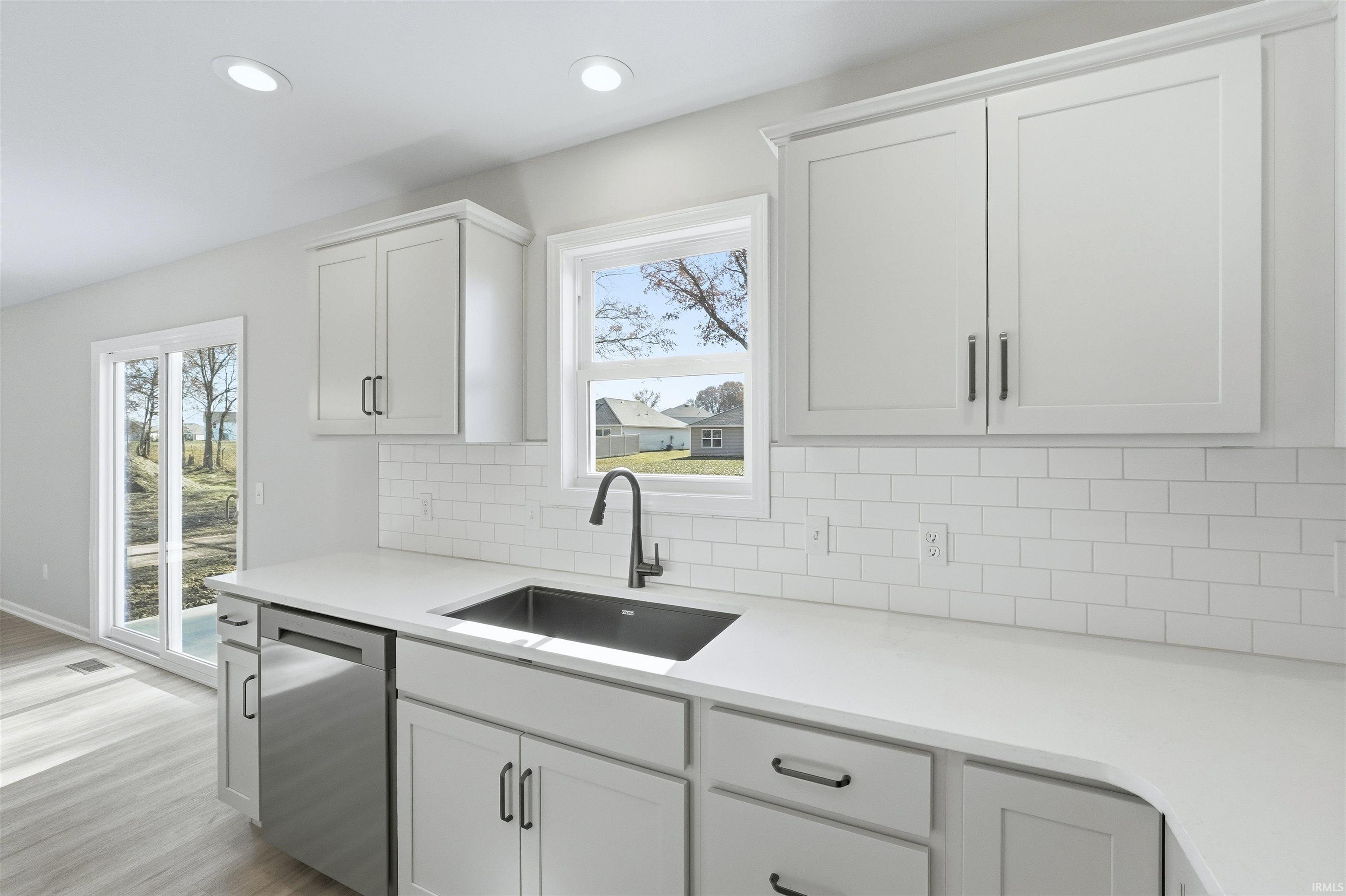 Kitchen featuring backsplash, dishwasher, white cabinetry, recessed lighting, and light wood-style flooring