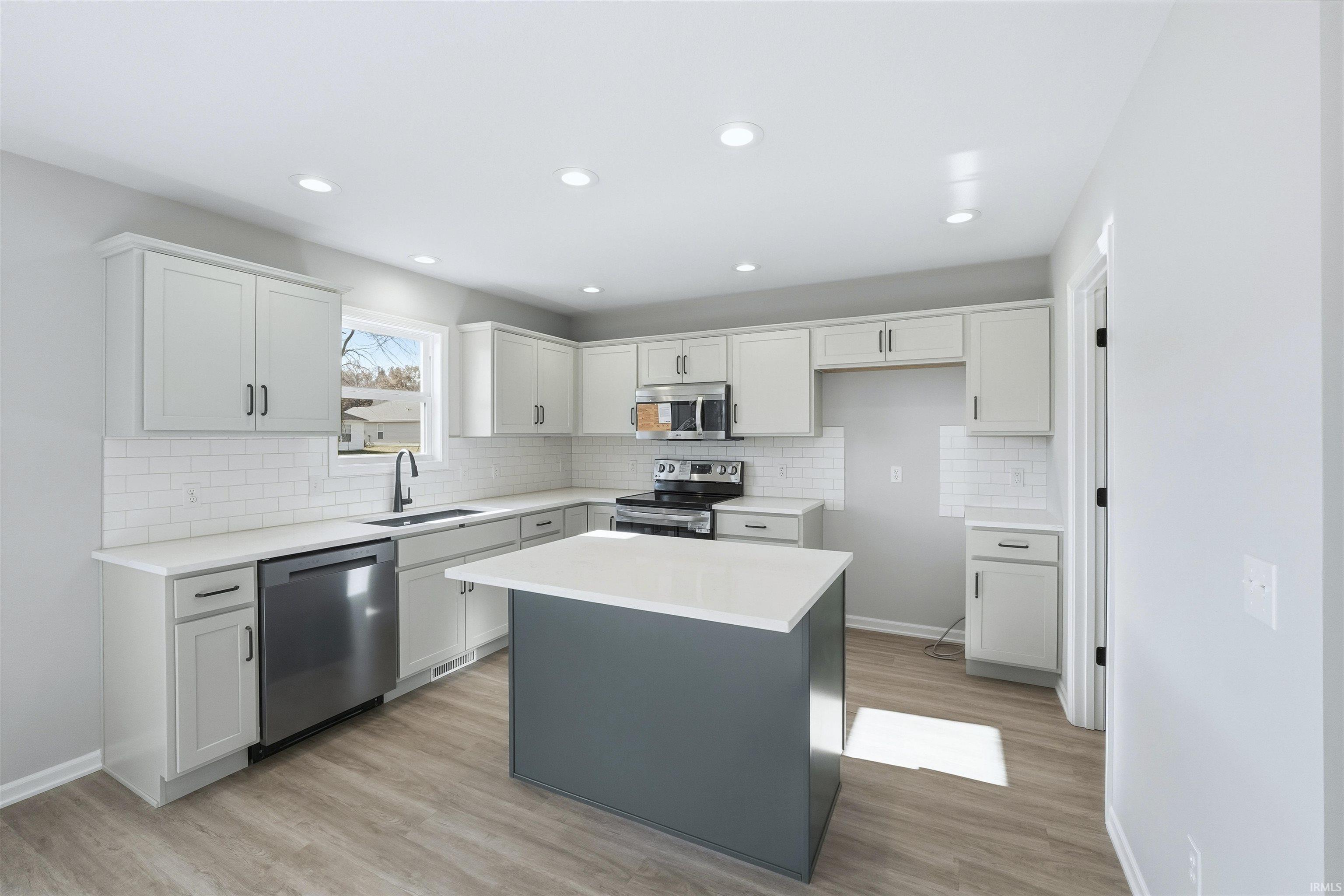Kitchen with white cabinetry, stainless steel appliances, a center island, backsplash, and light wood-style flooring