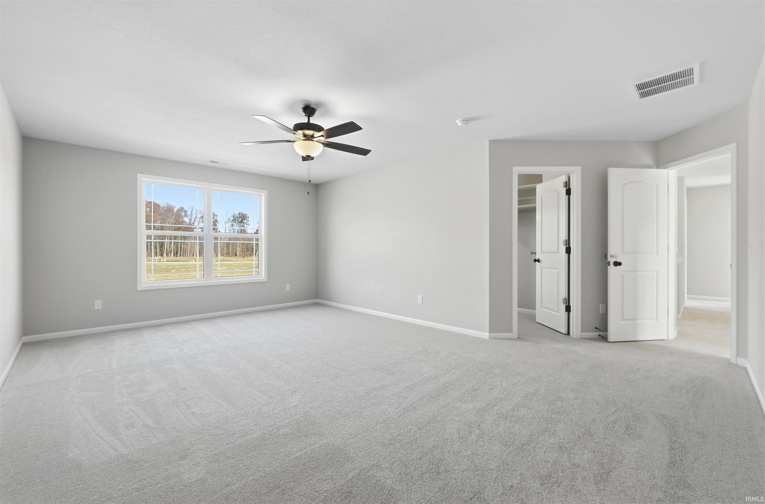 Unfurnished bedroom with a spacious closet, light carpet, and a ceiling fan