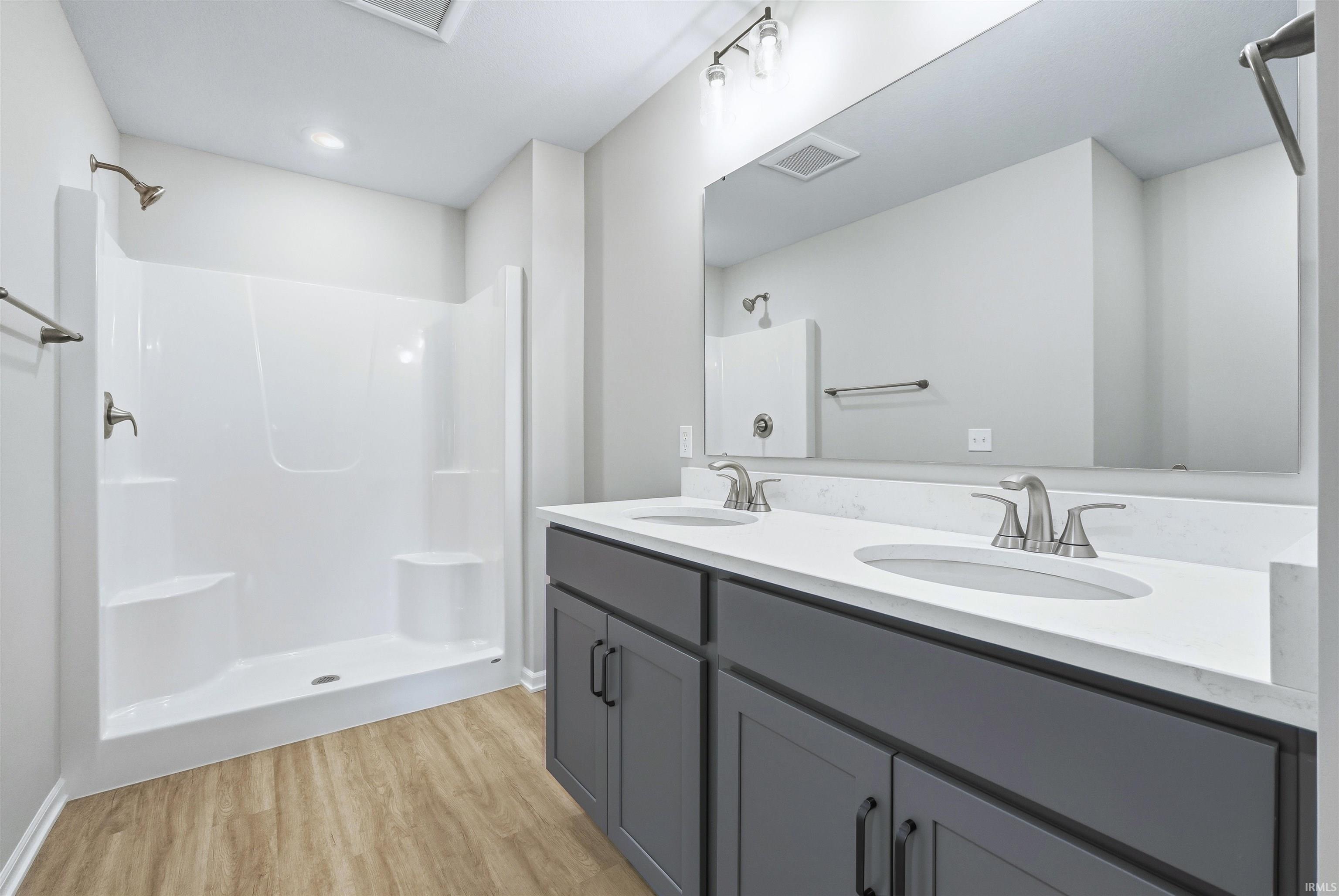Full bathroom featuring double vanity, a shower, and light wood-style floors