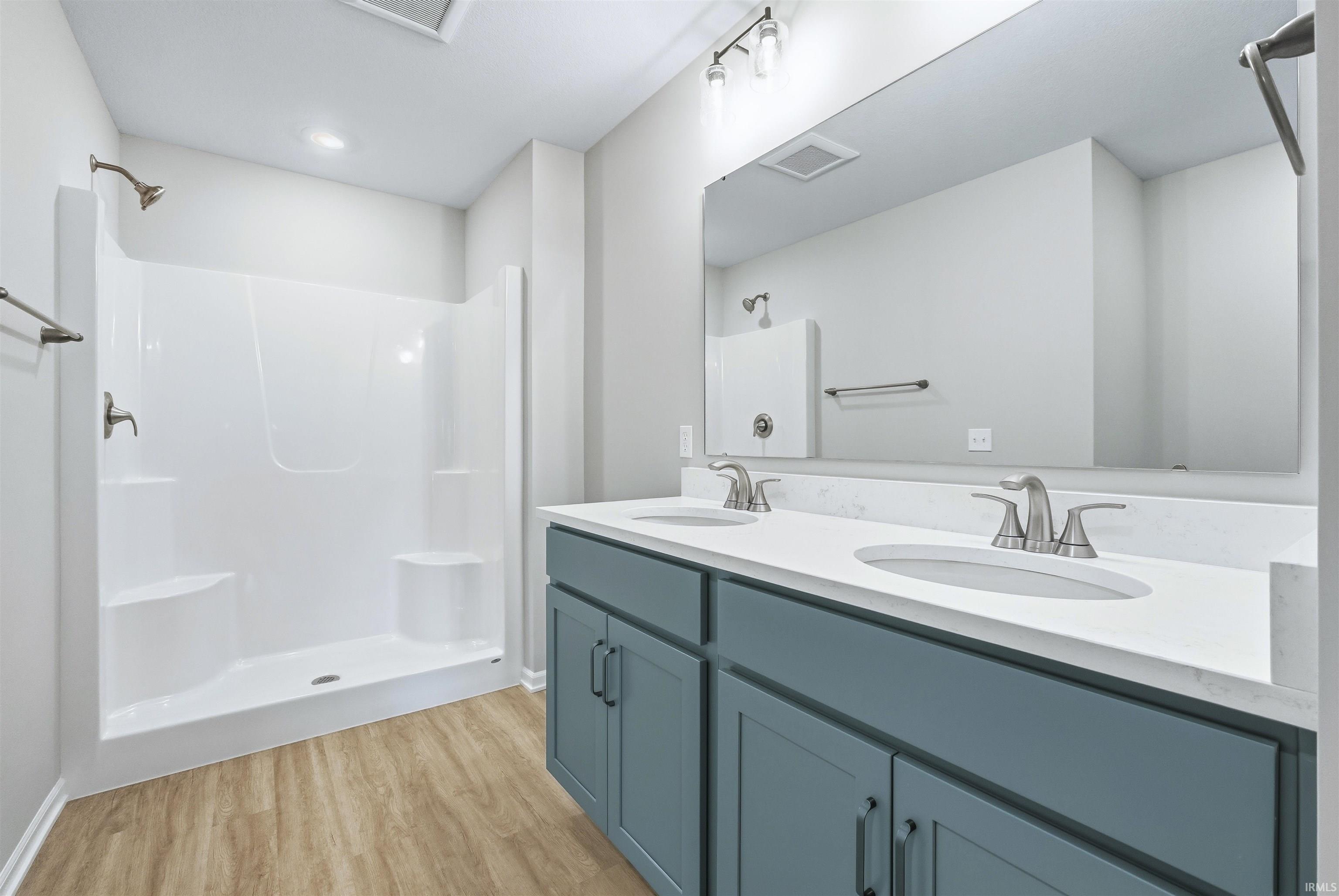 Bathroom with light wood-type flooring, double vanity, and a shower