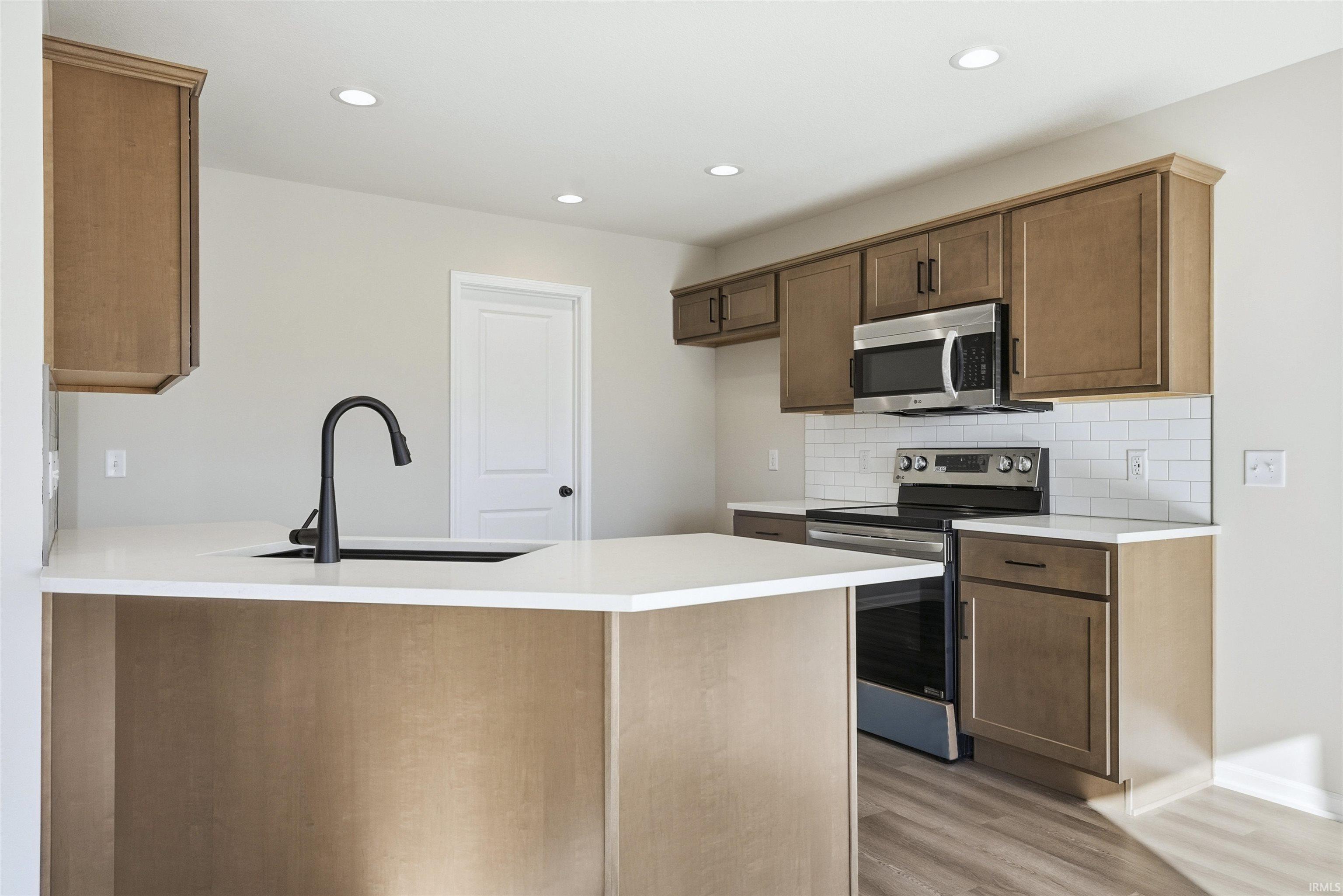 Kitchen with stainless steel appliances, a peninsula, recessed lighting, light wood-style floors, and backsplash