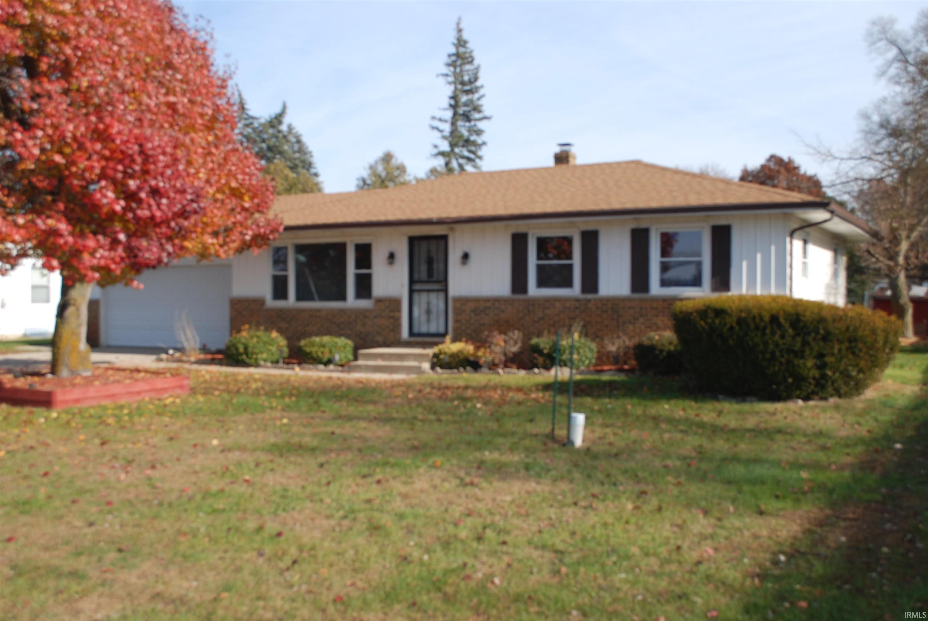 Ranch-style home featuring a front yard, brick siding, a chimney, and a garage