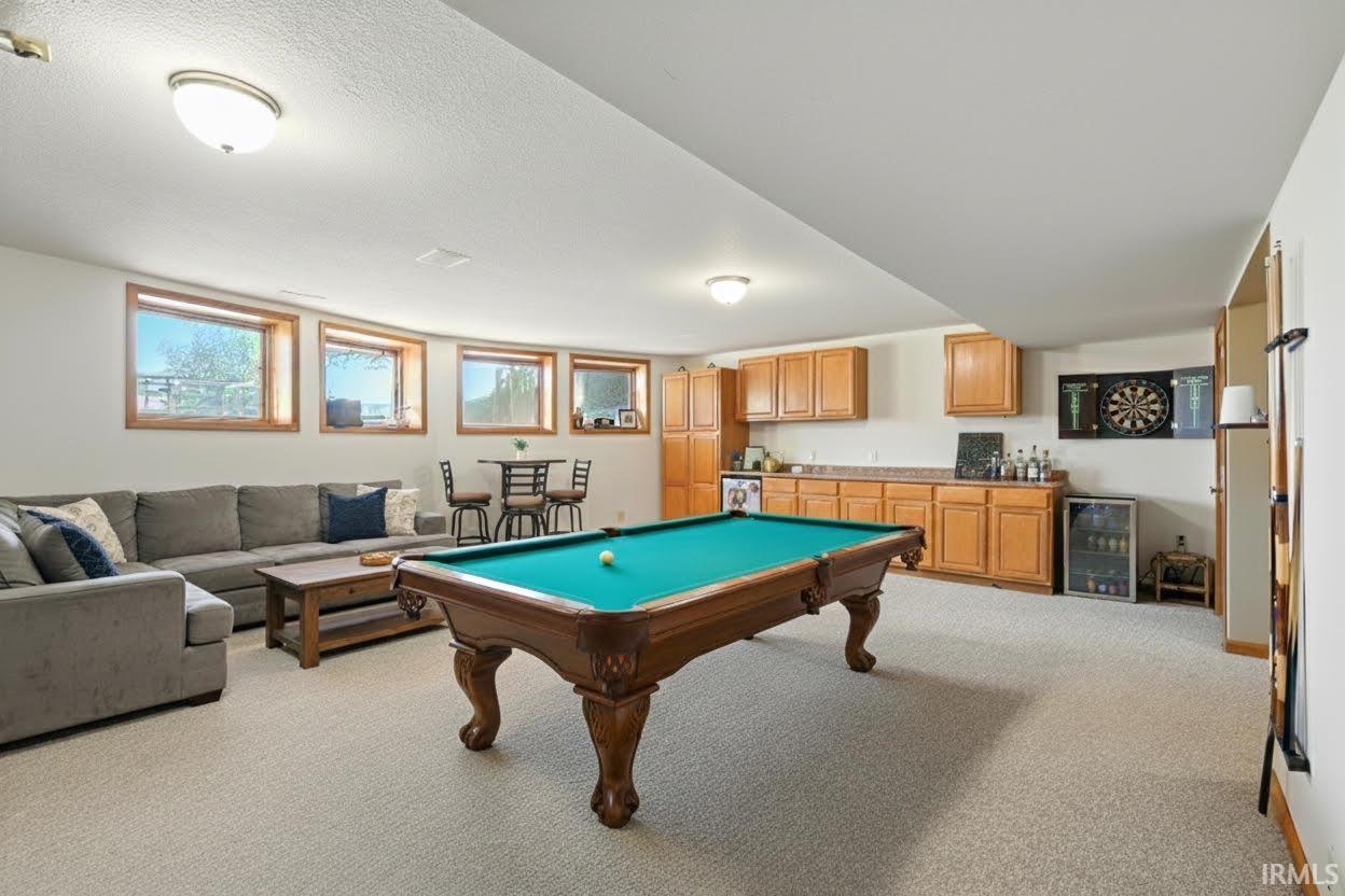 Game room with healthy amount of natural light, light carpet, wet bar, wine cooler, and a textured ceiling