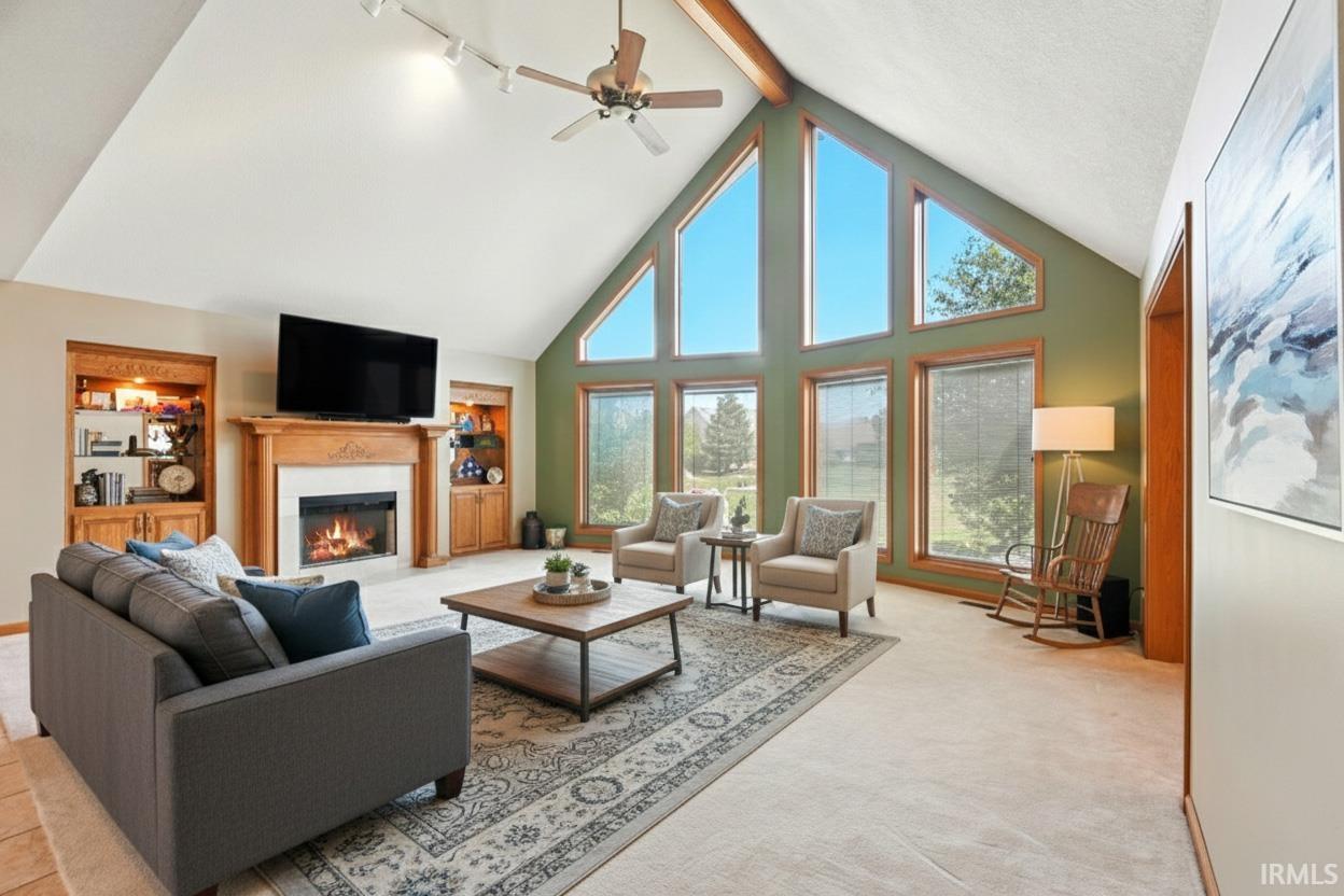 Living room featuring high vaulted ceiling, built in shelves, beamed ceiling, a glass covered fireplace, and light colored carpet