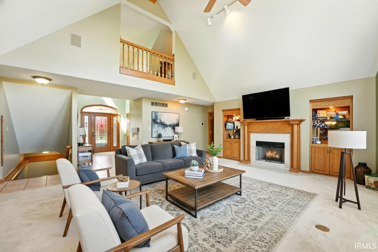 Carpeted living room with a fireplace with flush hearth, high vaulted ceiling, rail lighting, beam ceiling, and ceiling fan
