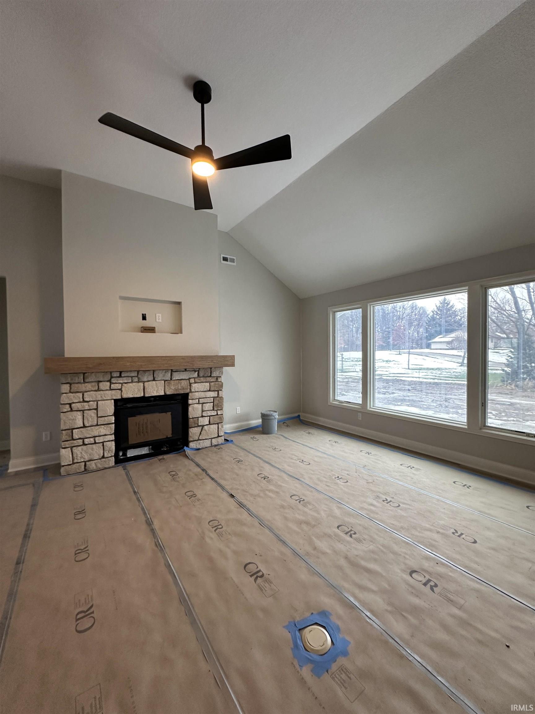 Unfurnished living room featuring a fireplace, lofted ceiling, and a ceiling fan