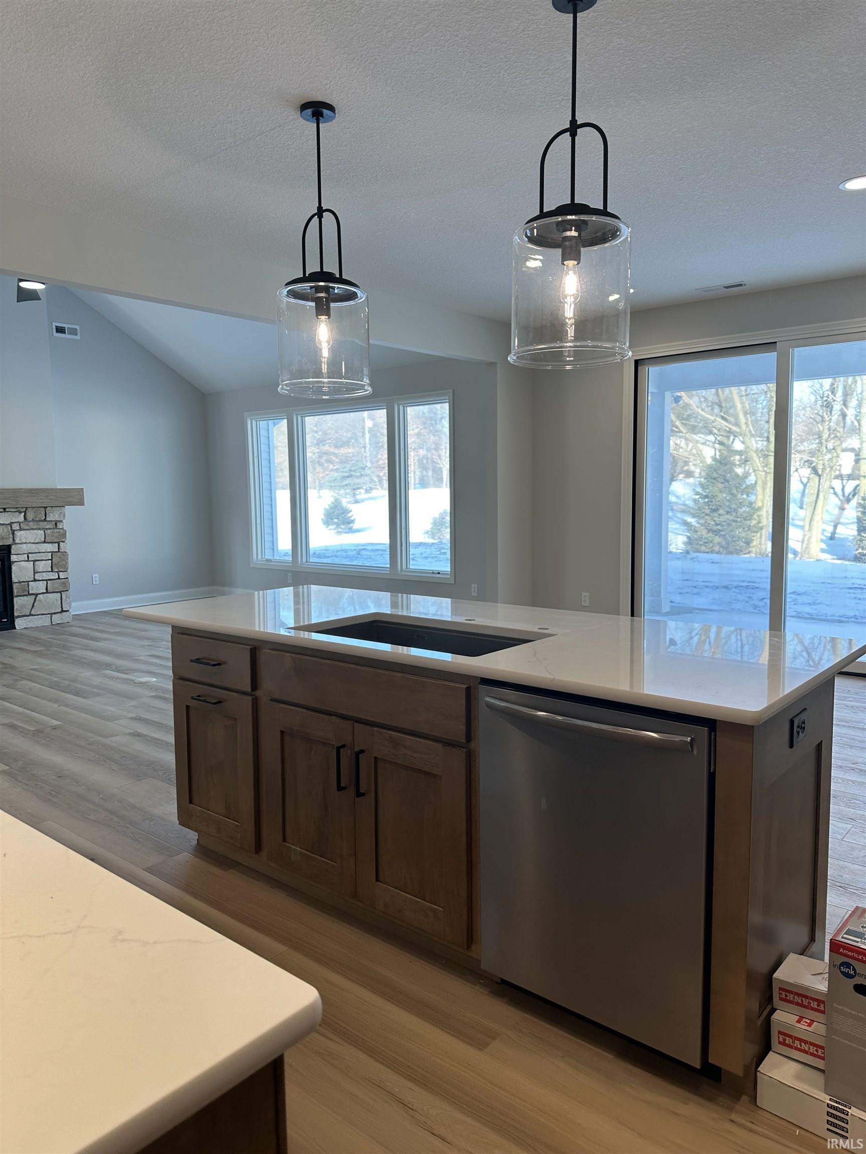 Kitchen featuring light wood-style floors, hanging light fixtures, dishwasher, open floor plan, and vaulted ceiling