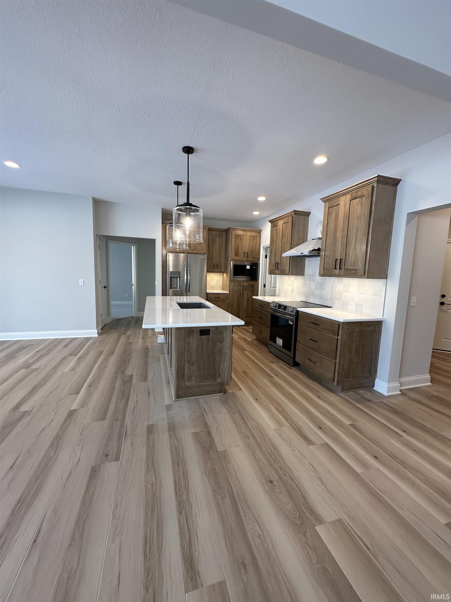 Kitchen featuring hanging light fixtures, recessed lighting, a center island with sink, appliances with stainless steel finishes, and light wood-type flooring