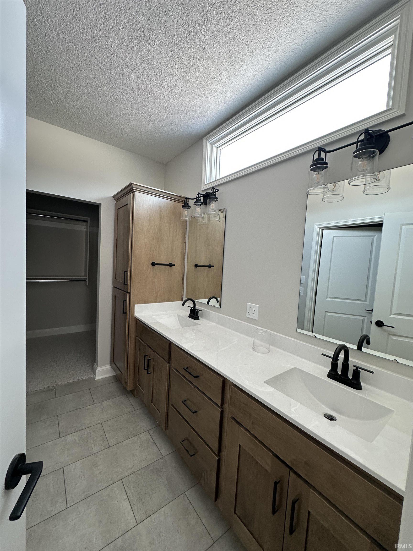 Full bathroom with double vanity, a textured ceiling, and light tile patterned floors