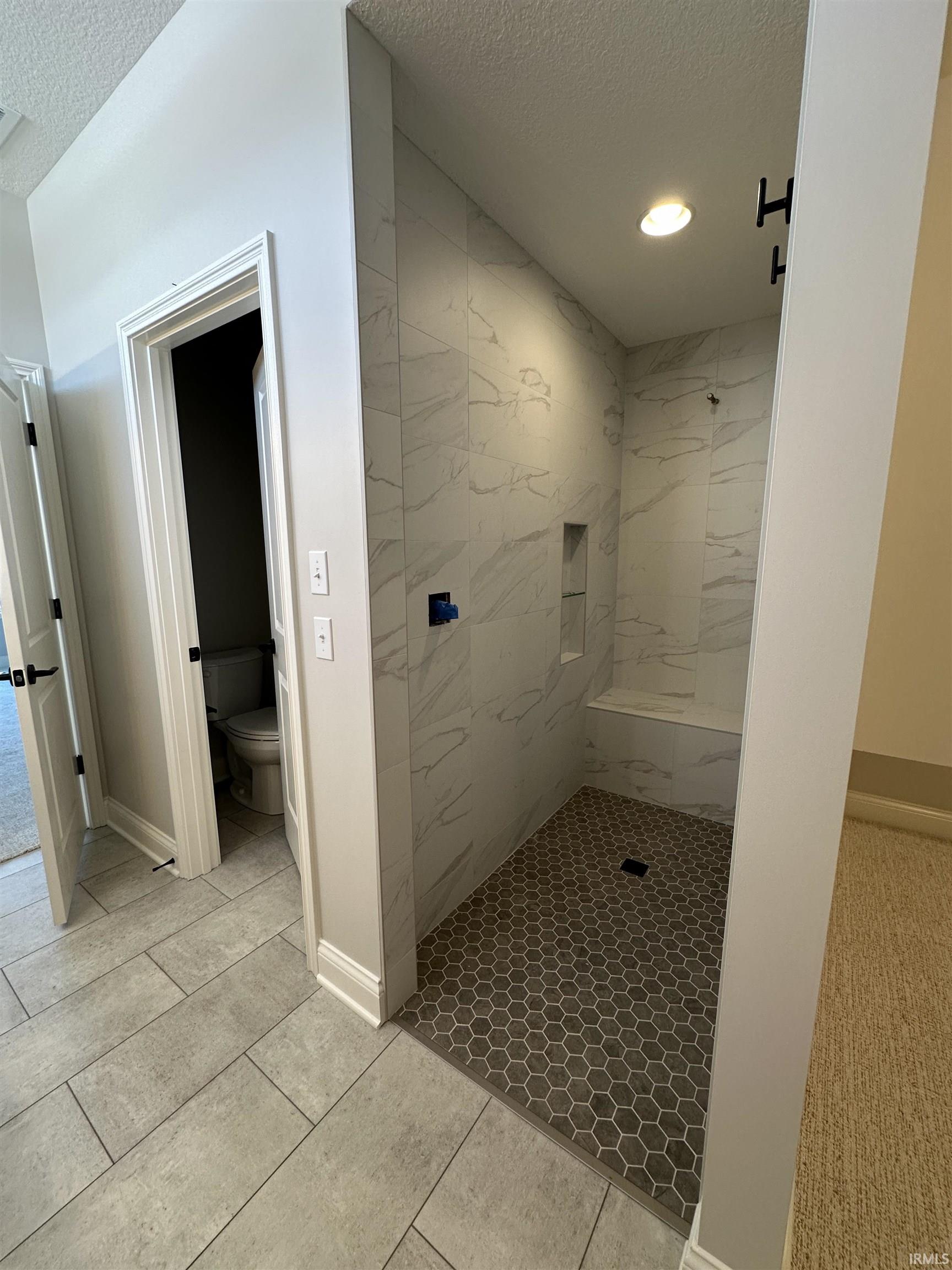 Full bathroom with a textured ceiling, a marble finish shower, and light tile patterned floors