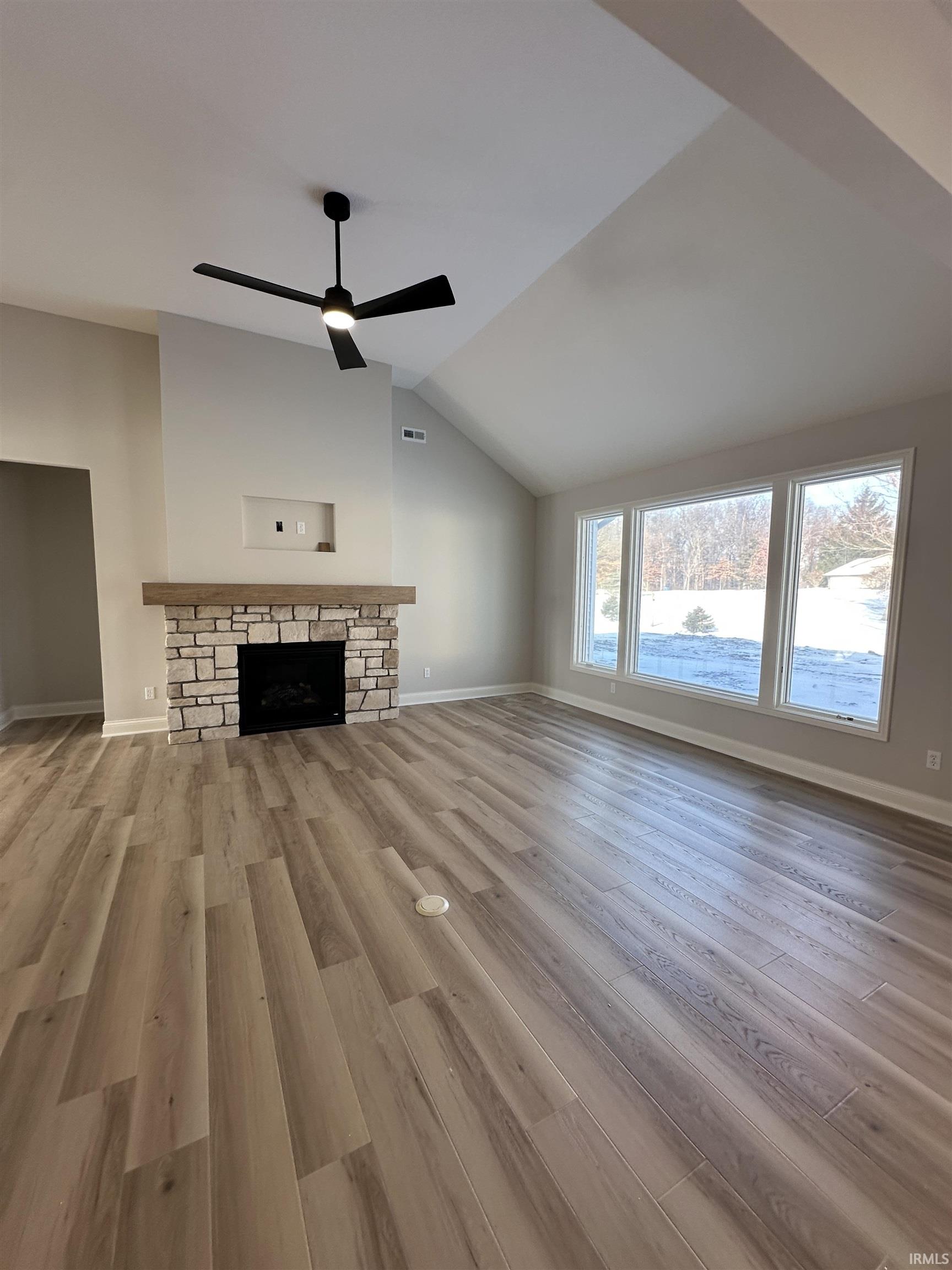 Unfurnished living room with a fireplace, light wood-type flooring, lofted ceiling, and ceiling fan