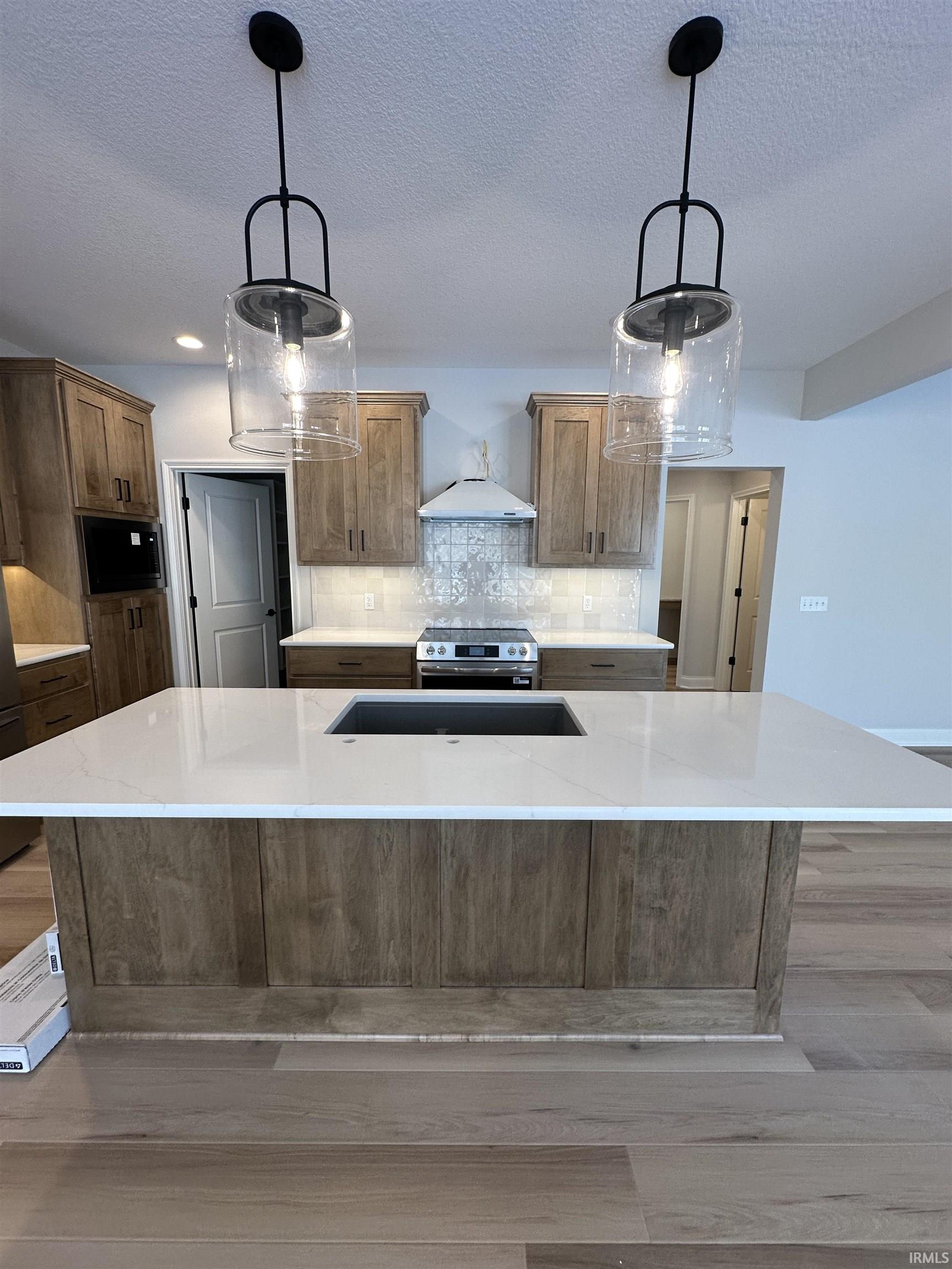 Kitchen featuring an island with sink, light stone counters, pendant lighting, backsplash, and electric range
