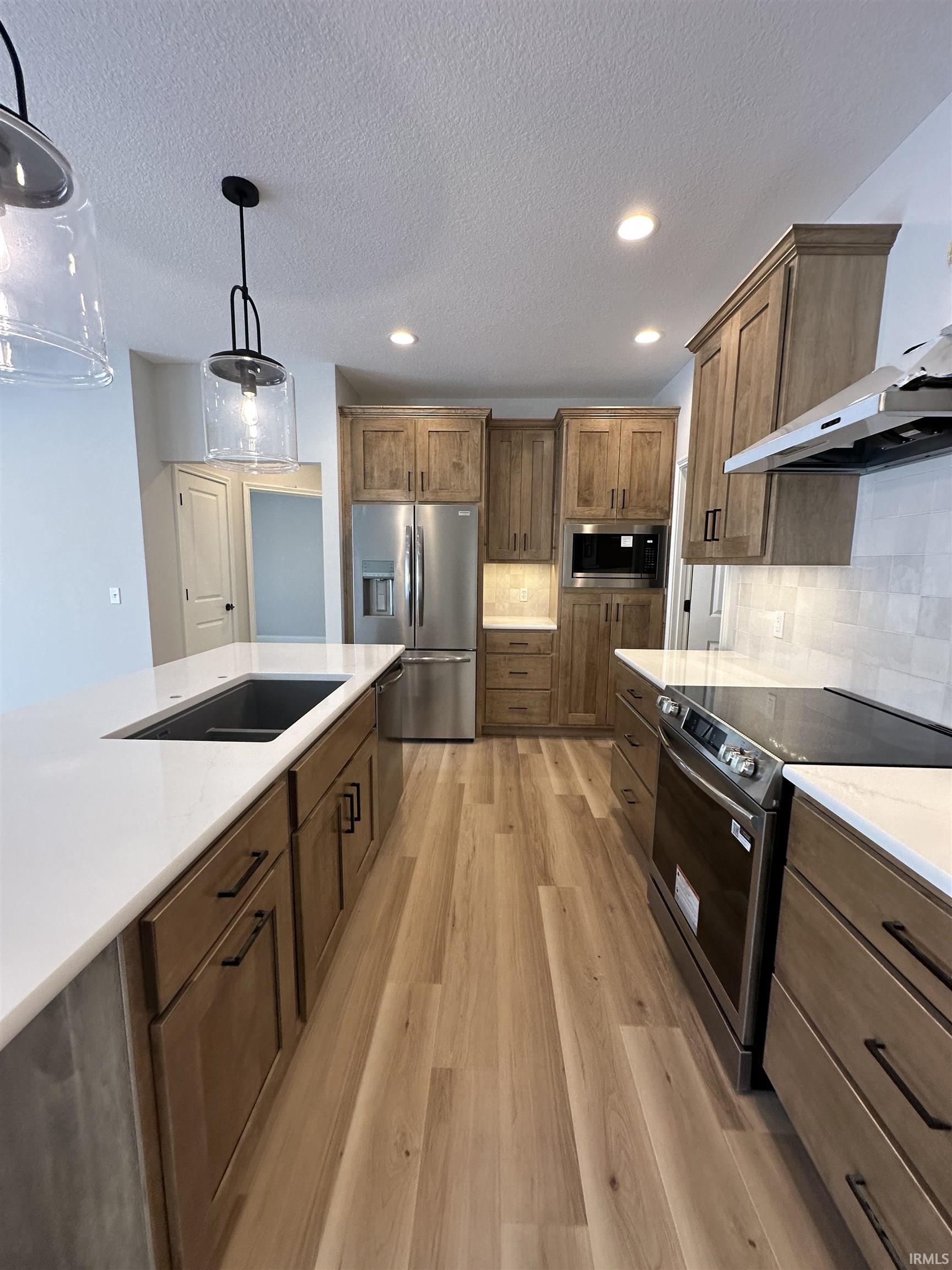 Kitchen with stainless steel appliances, pendant lighting, recessed lighting, a textured ceiling, and light wood-style flooring