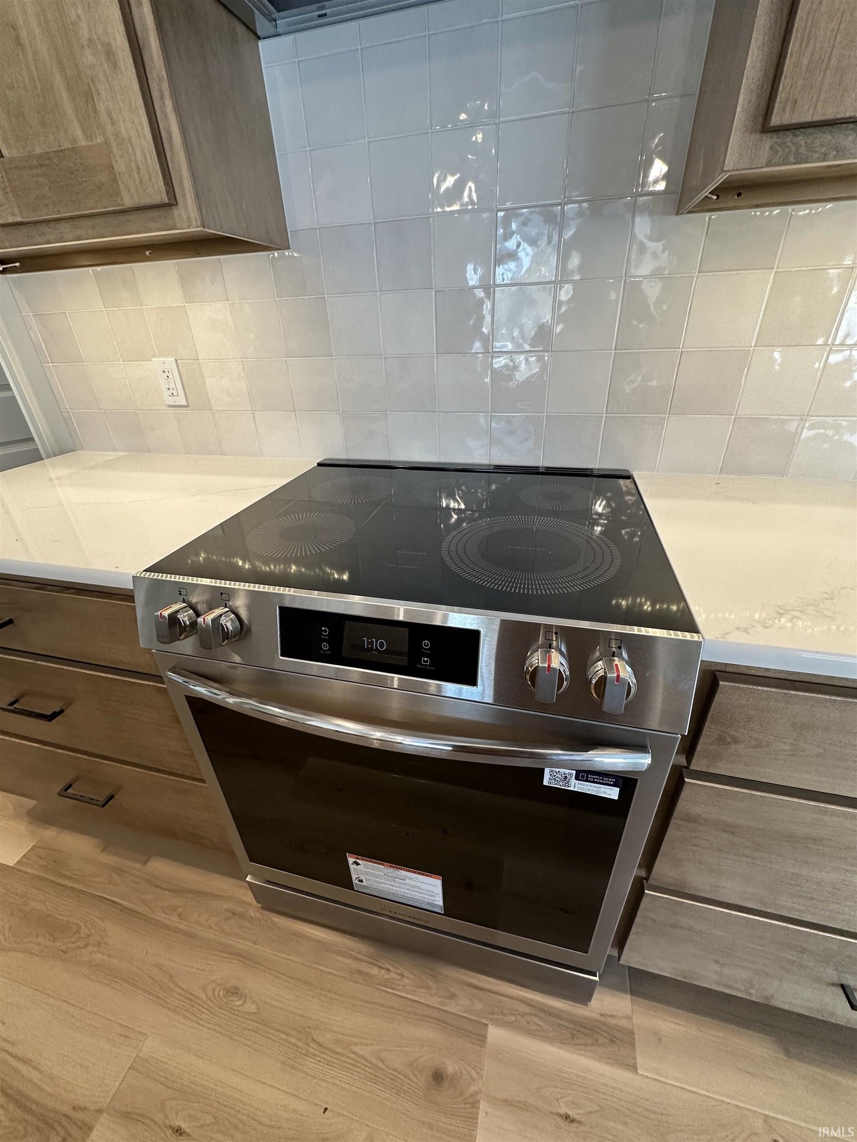 Kitchen view of backsplash, stainless steel electric range oven, light stone countertops, and light wood-type flooring