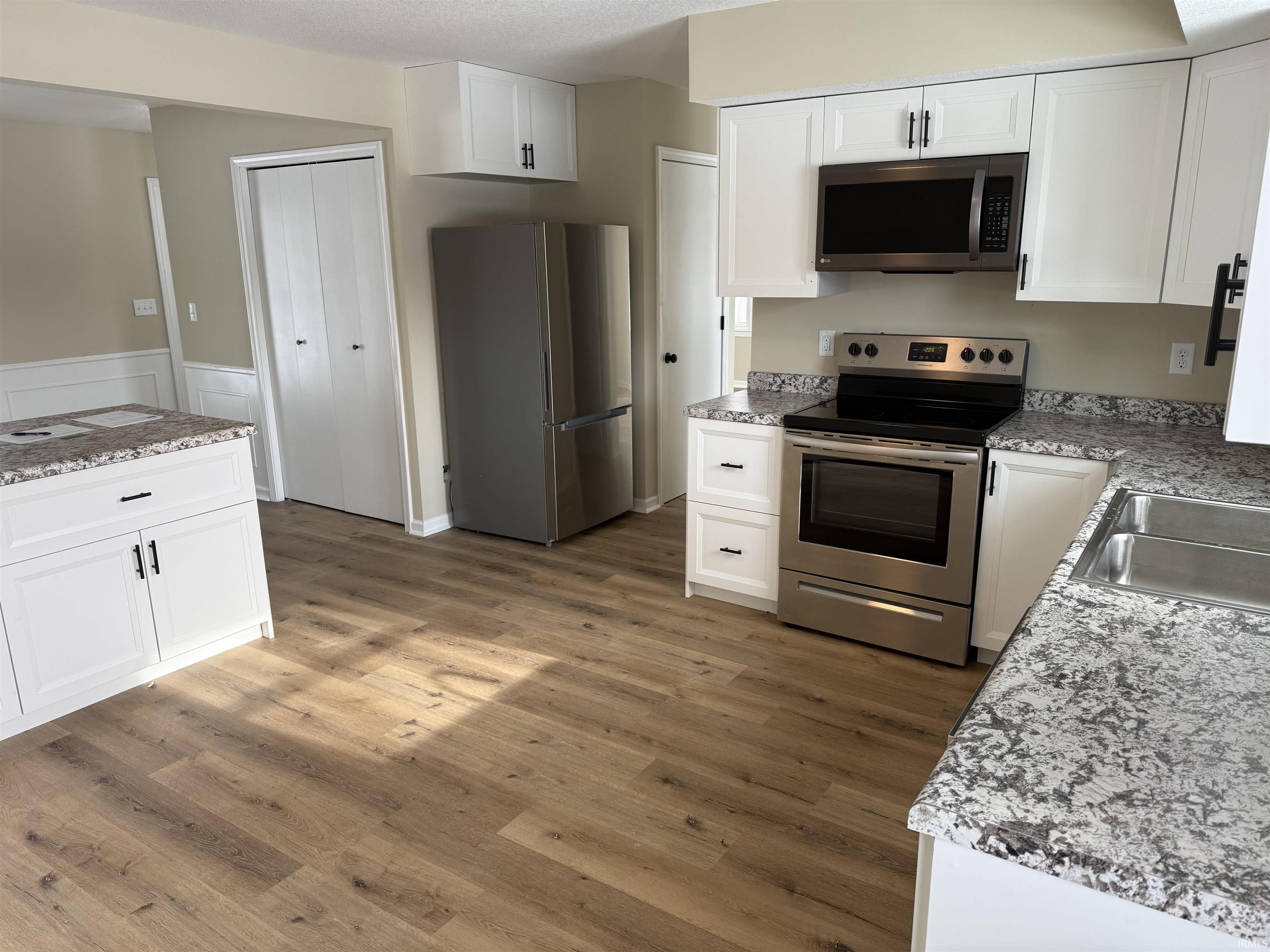 Kitchen featuring appliances with stainless steel finishes, white cabinets, vinyl plank floors.