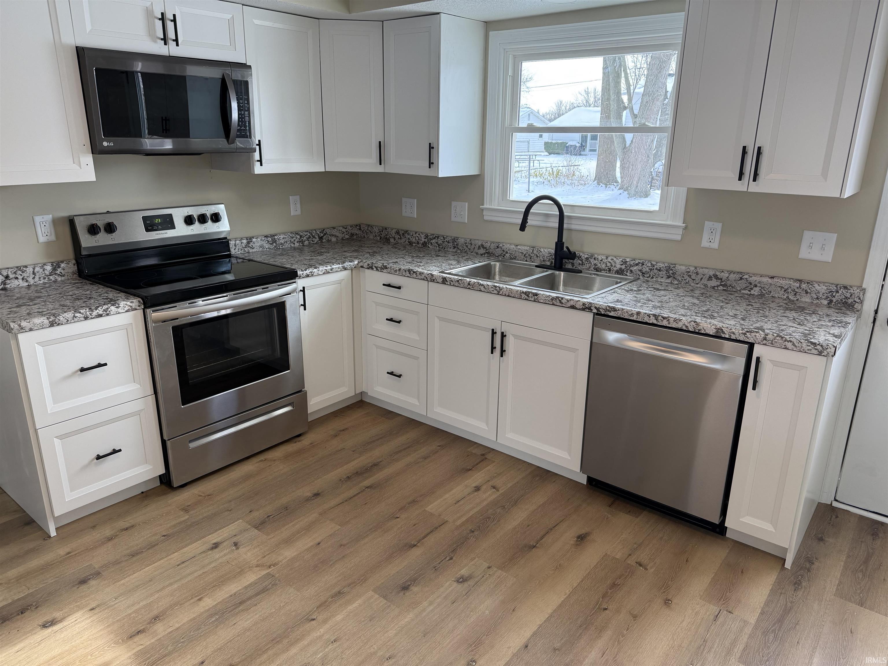 Kitchen featuring stainless steel appliances, white cabinetry, light vinyl plank flooring.