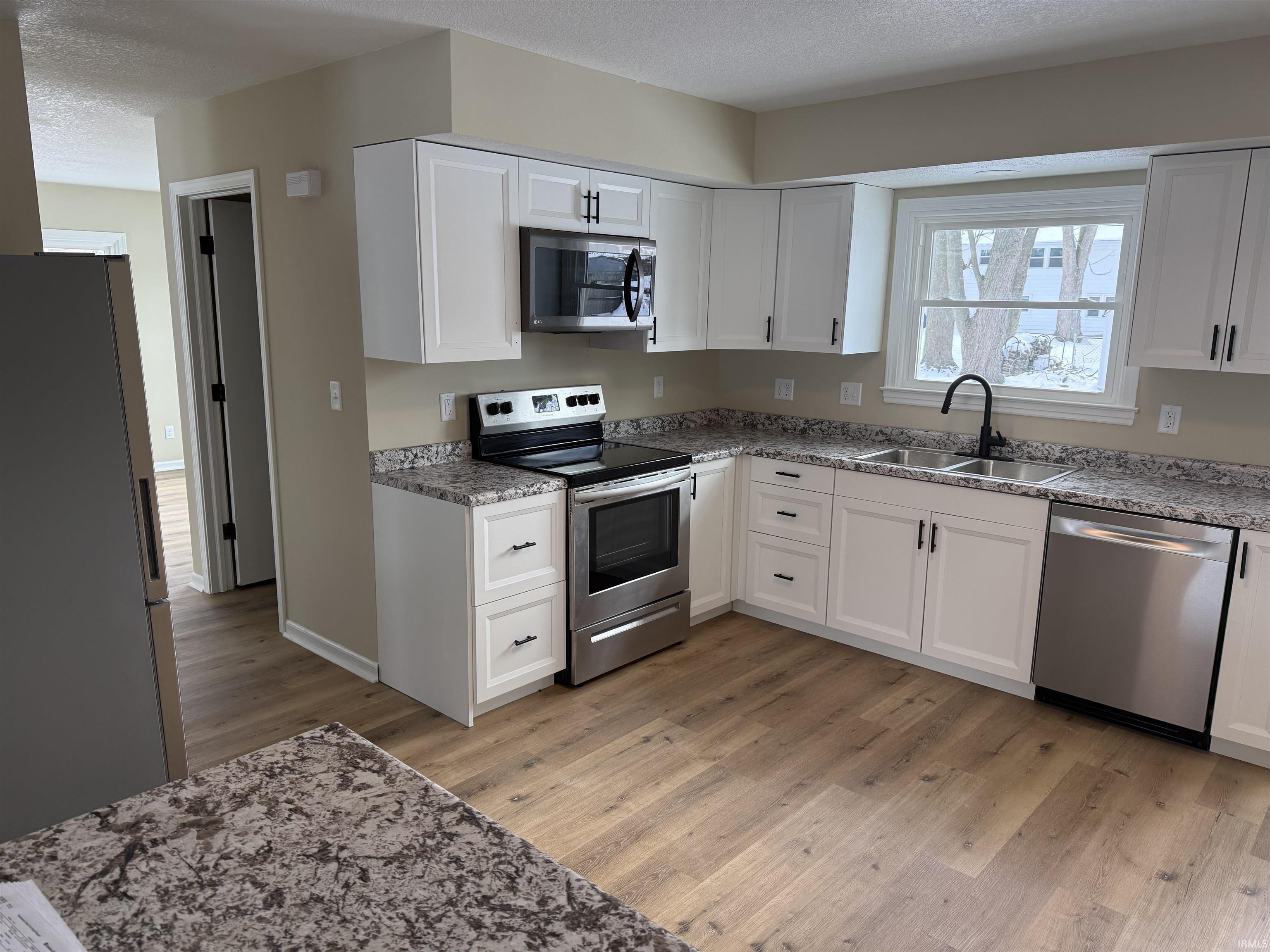 Kitchen featuring appliances with stainless steel finishes, white cabinetry, light wood-style flooring, Spanish laced ceilings.