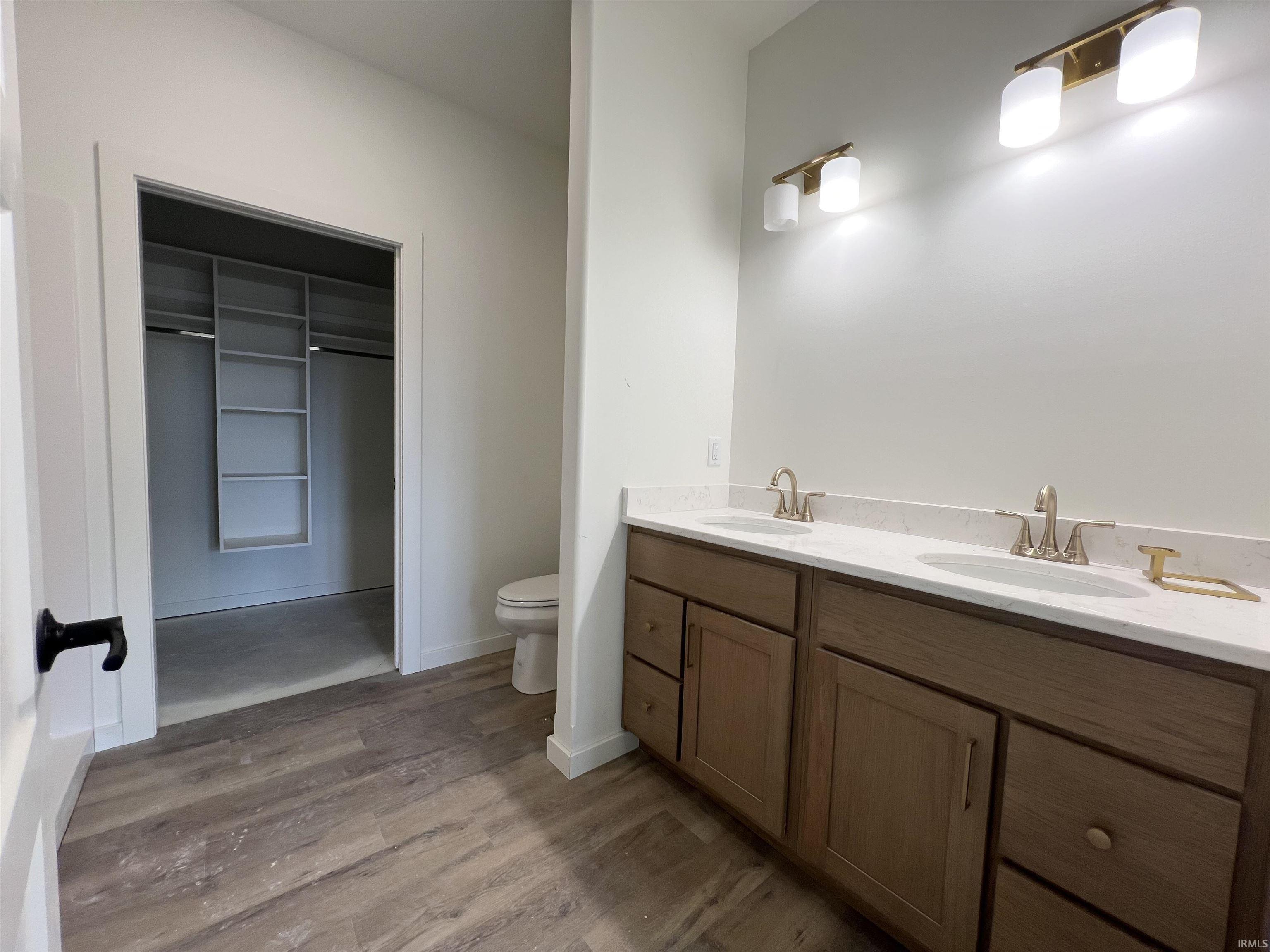 Full bath featuring double vanity, a spacious closet, and light wood-style floors