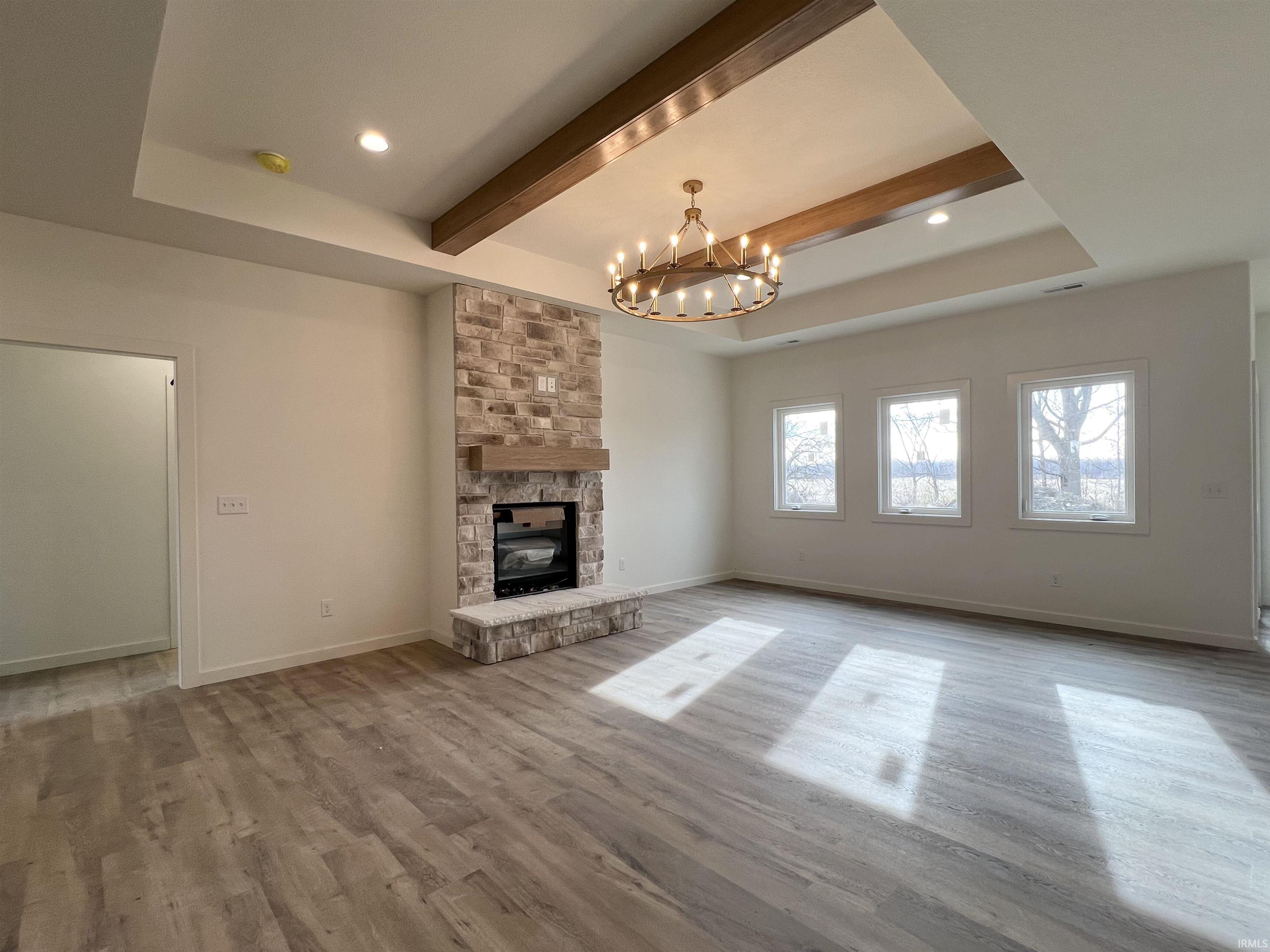 Unfurnished living room with light wood-style floors, a stone fireplace, a chandelier, recessed lighting, and a raised ceiling