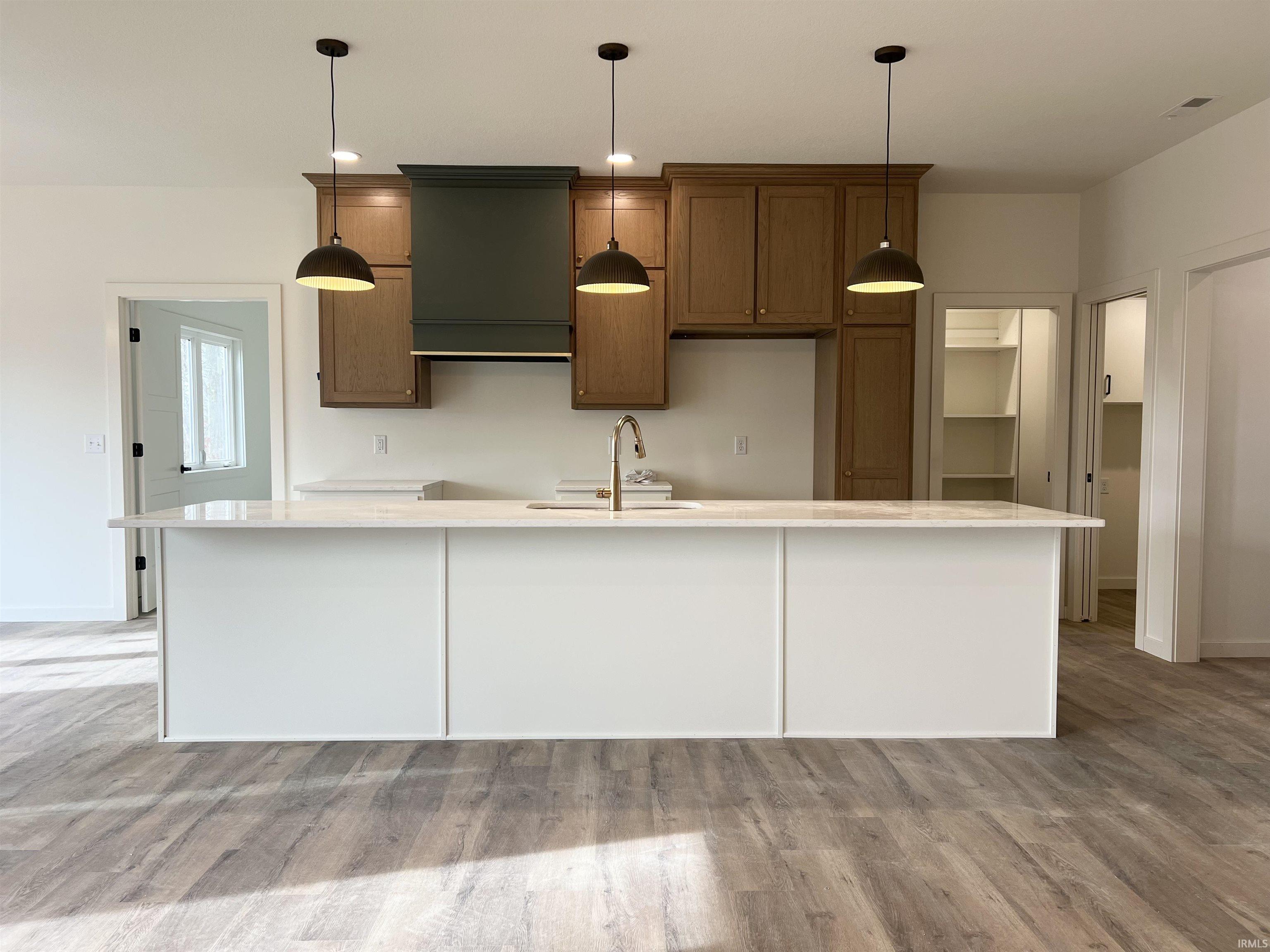 Kitchen featuring light wood-type flooring, hanging light fixtures, an island with sink, and light stone countertops