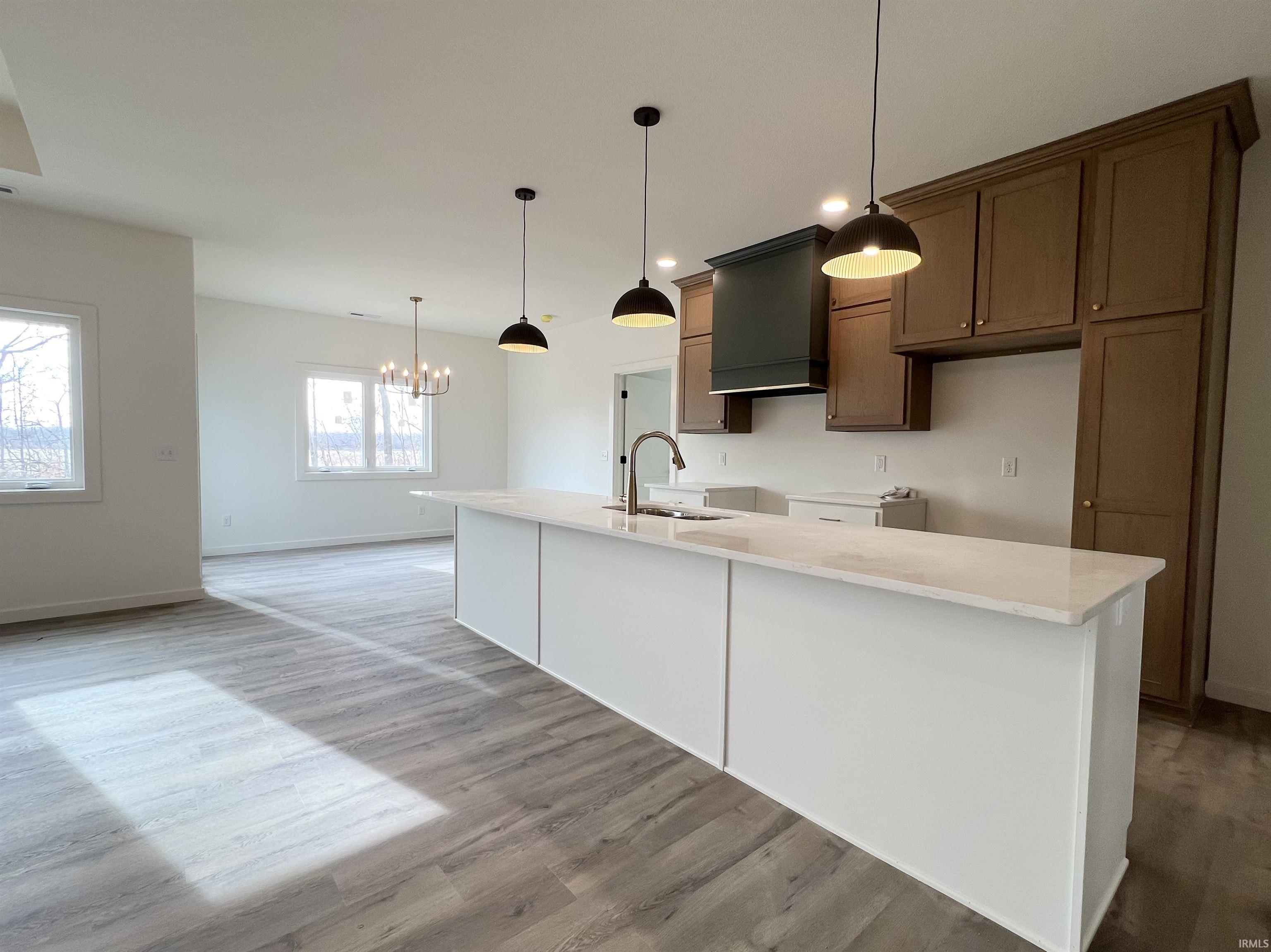Kitchen with decorative light fixtures, an island with sink, light stone countertops, a chandelier, and recessed lighting
