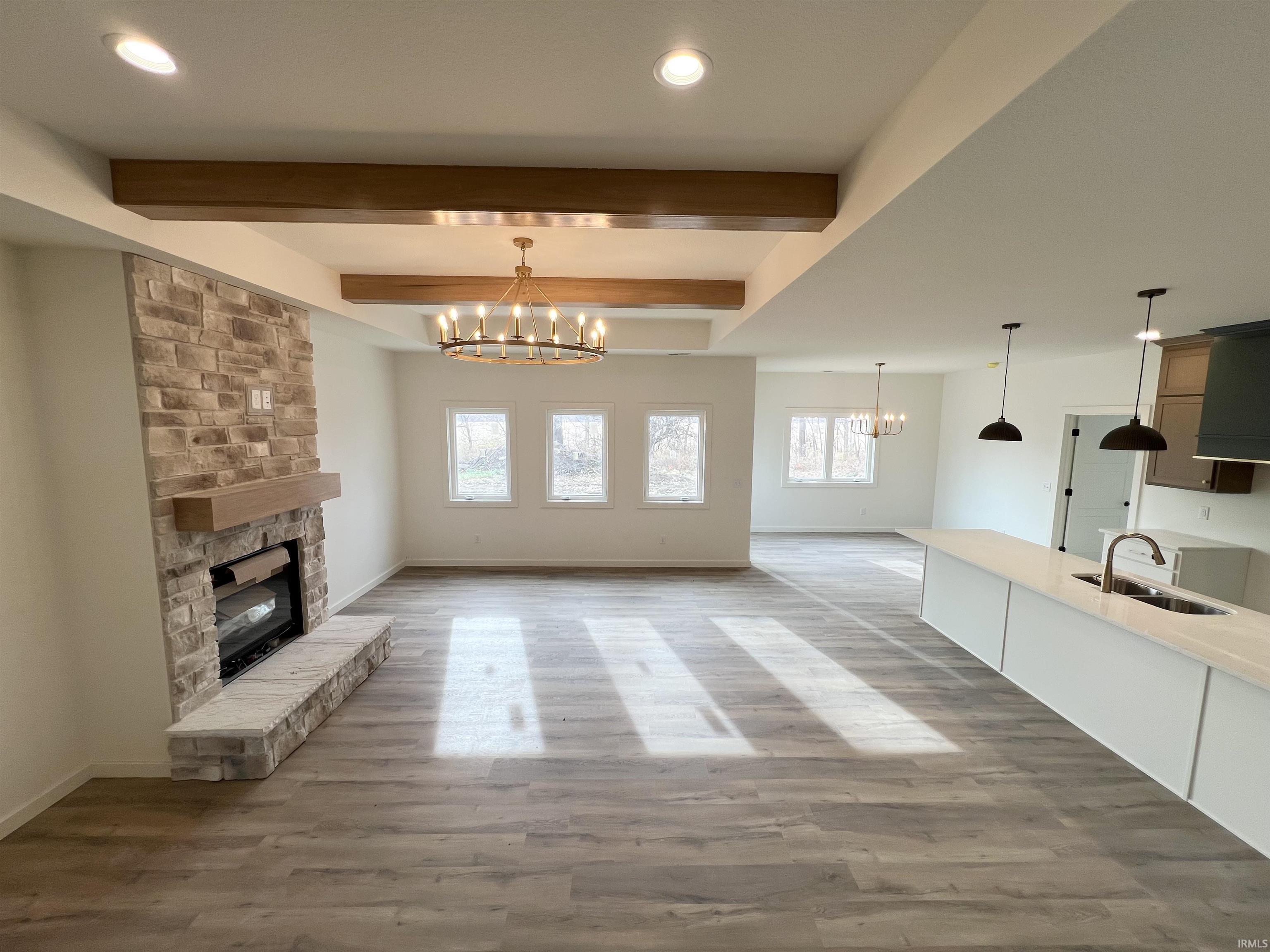 Unfurnished living room with a stone fireplace, a chandelier, beam ceiling, light wood-type flooring, and recessed lighting