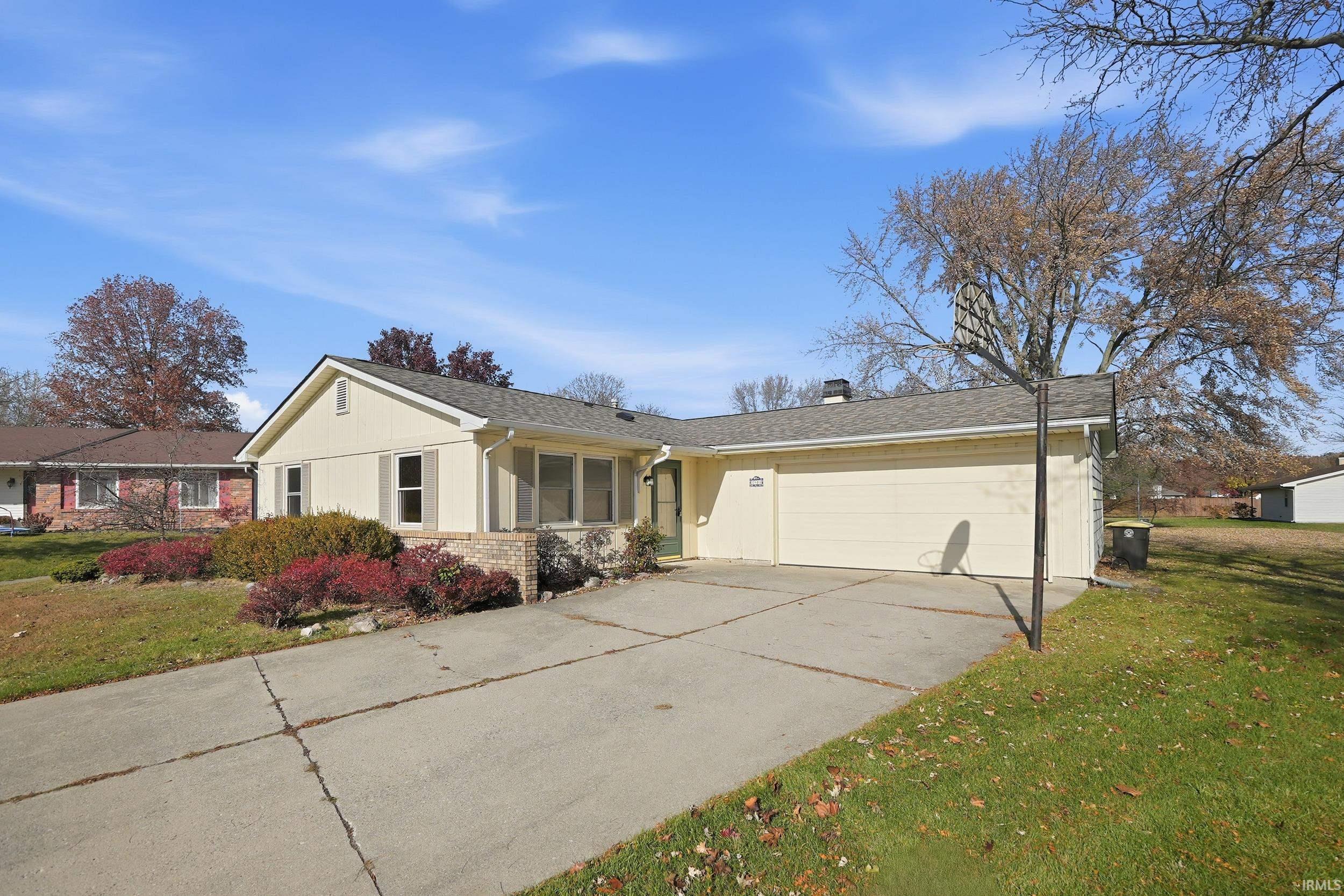 View of front of property featuring a front lawn, driveway, brick siding, a chimney, and an attached garage
