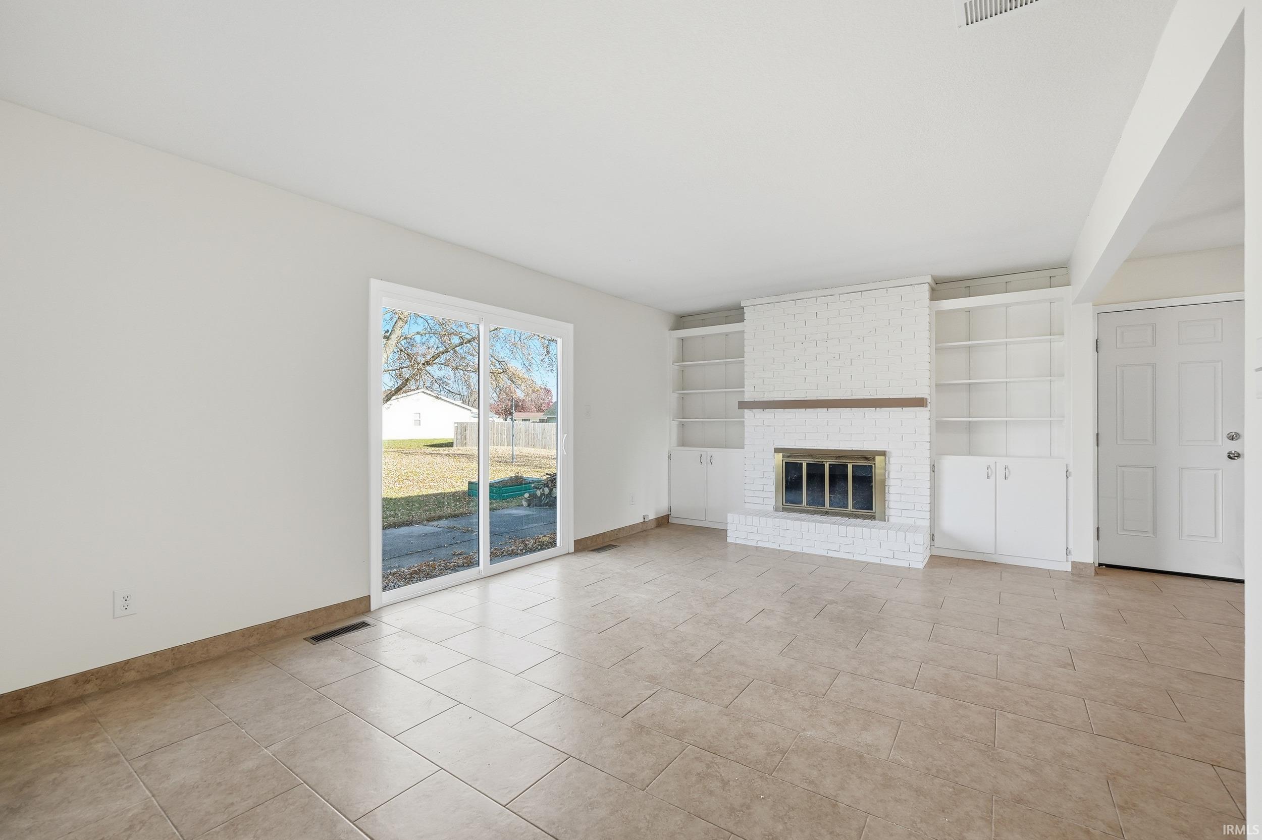 Unfurnished living room featuring a brick fireplace, built in features, and light tile patterned flooring