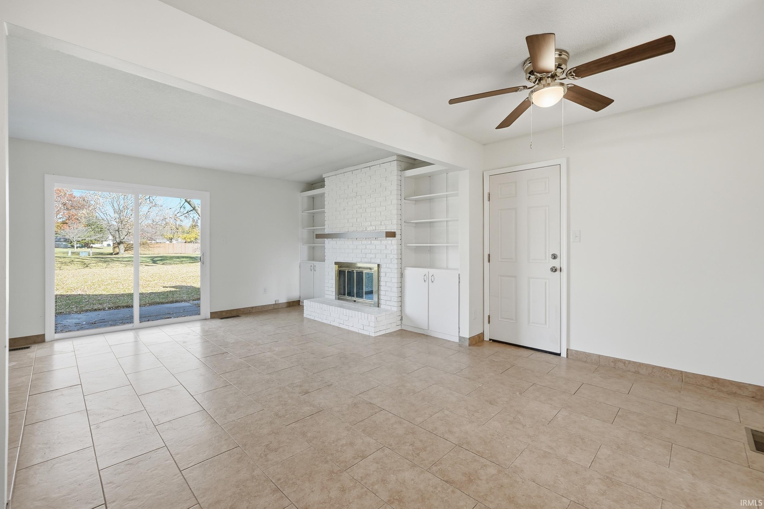 Unfurnished living room with built in shelves, a fireplace, a ceiling fan, and light tile patterned floors